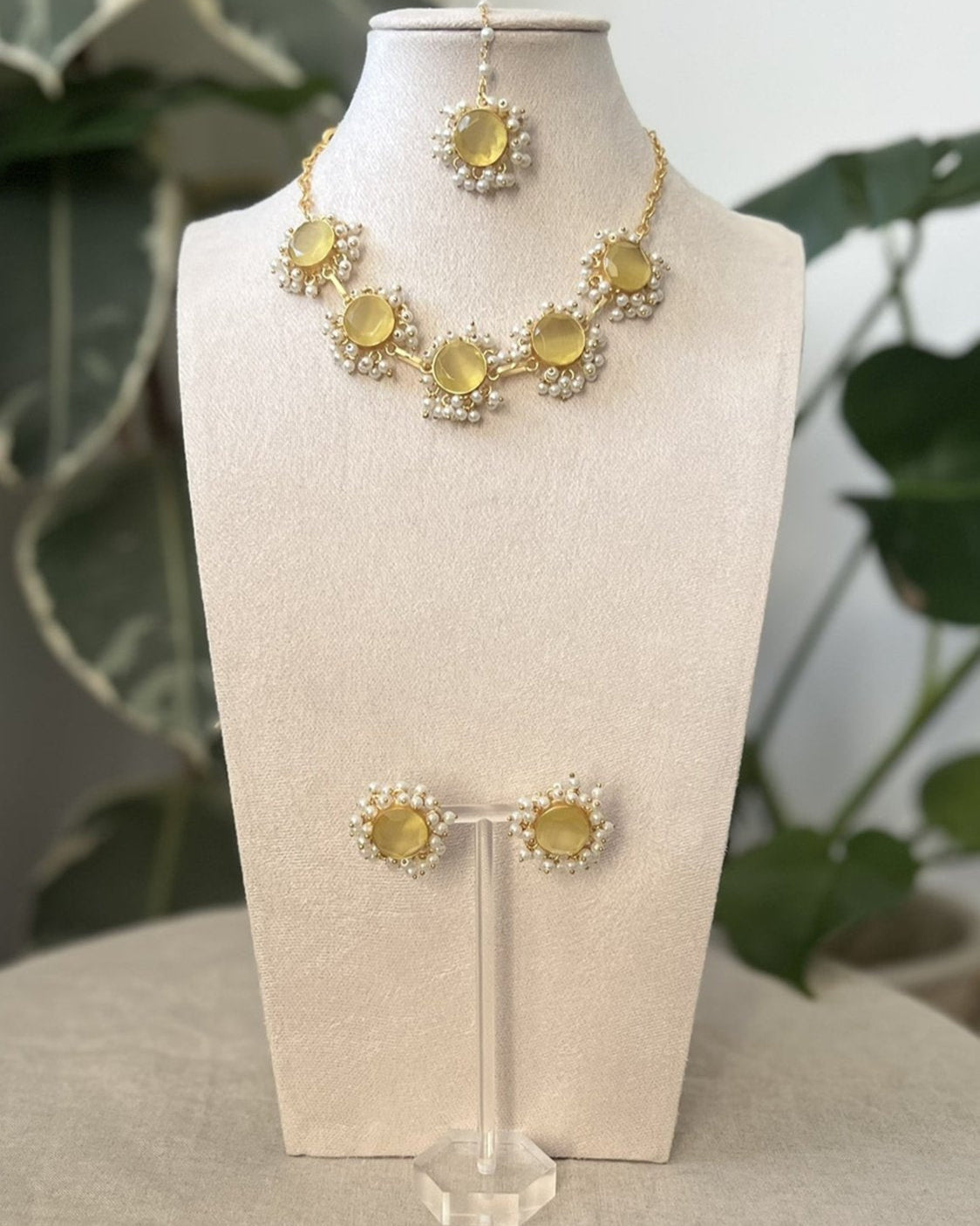 A jewelry set featuring a necklace and earrings with a central citrine semi-precious stone surrounded by clusters of mini pearls, displayed on a mannequin bust.