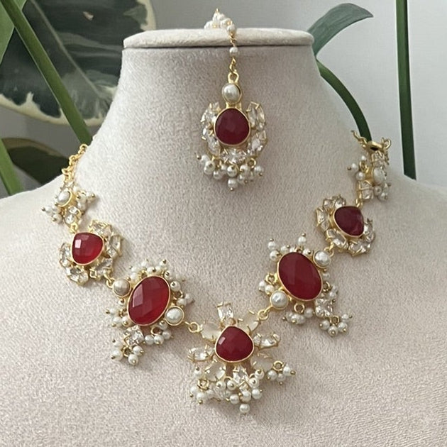 Red ruby and pearls indian jewelry set with necklace and earrings on a white stand with green leaves in the background