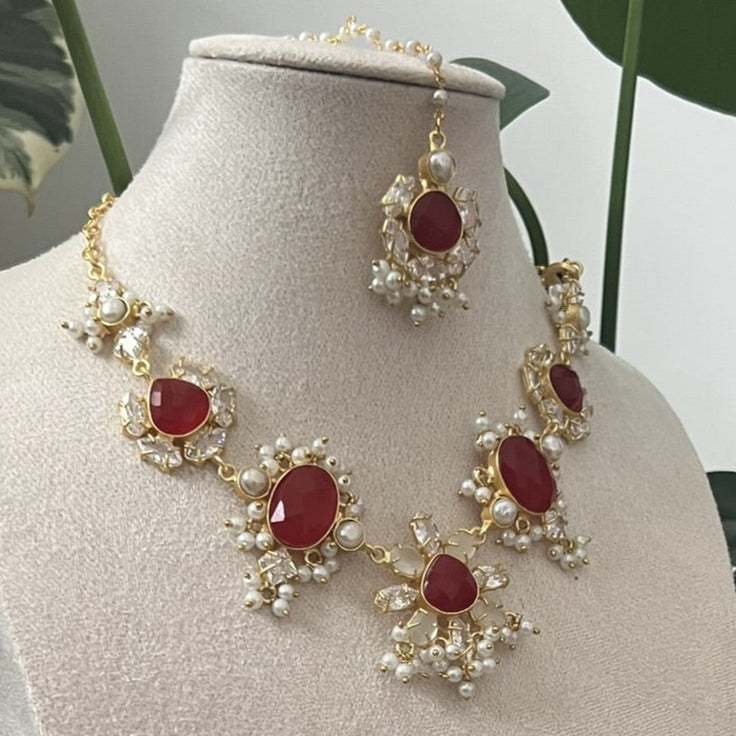 Red ruby and pearls indian jewelry set with necklace and earrings on a white stand with green leaves in the background