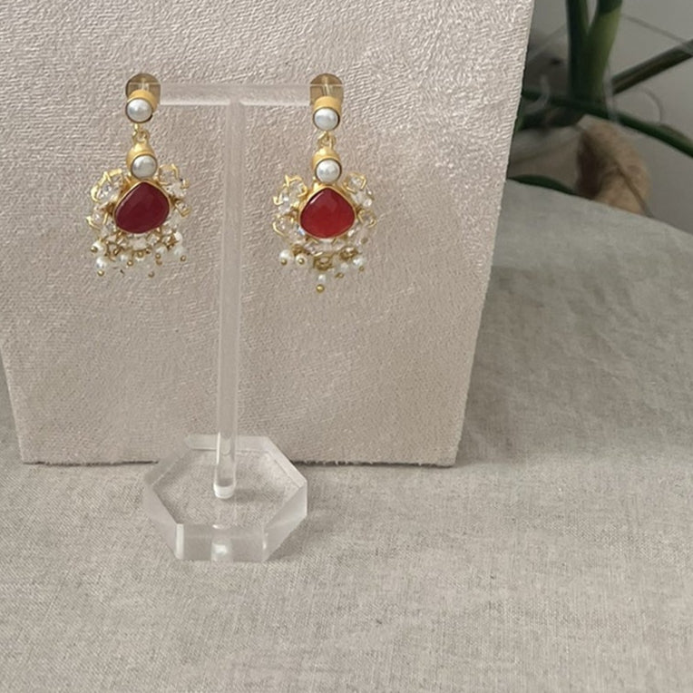 Red ruby and pearls indian jewelry set with necklace and earrings on a white stand with green leaves in the background