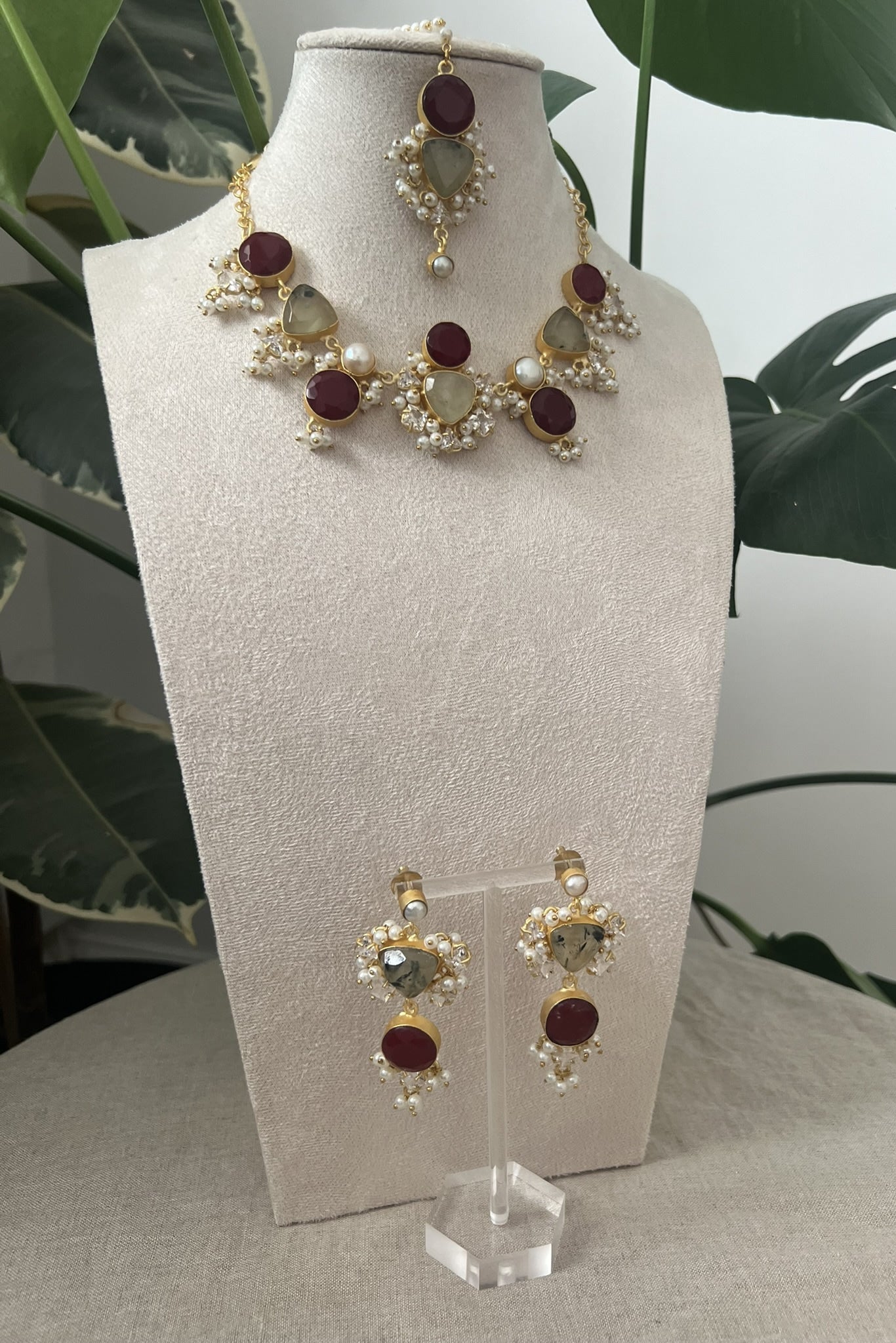 Jewelry set on a white stand with a plant in the background