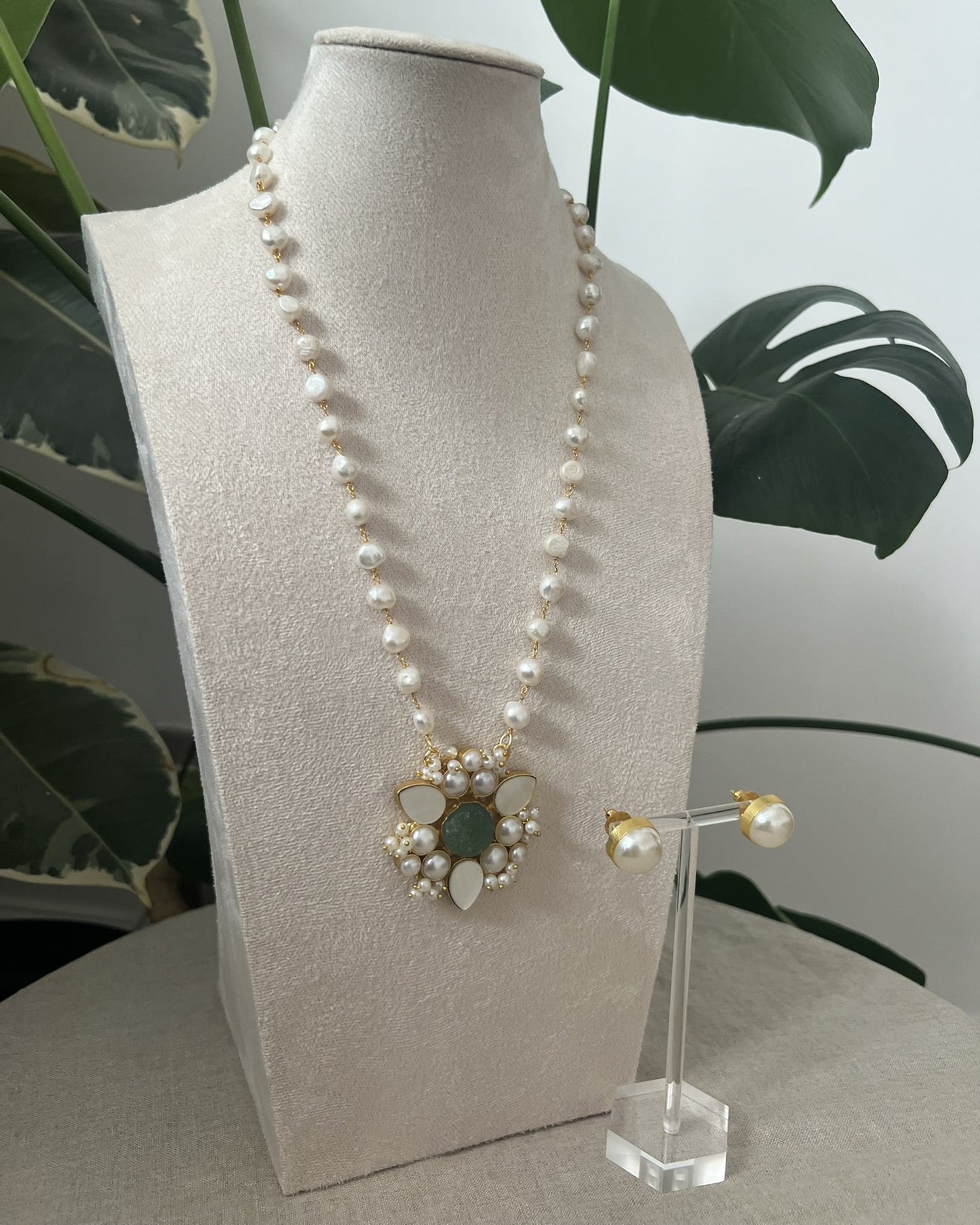 Pearl necklace with a decorative clasp on a mannequin bust, with a plant in the background.