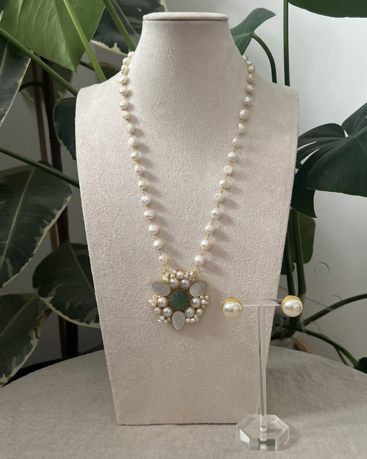 Pearl necklace on a mannequin bust with a plant in the background
