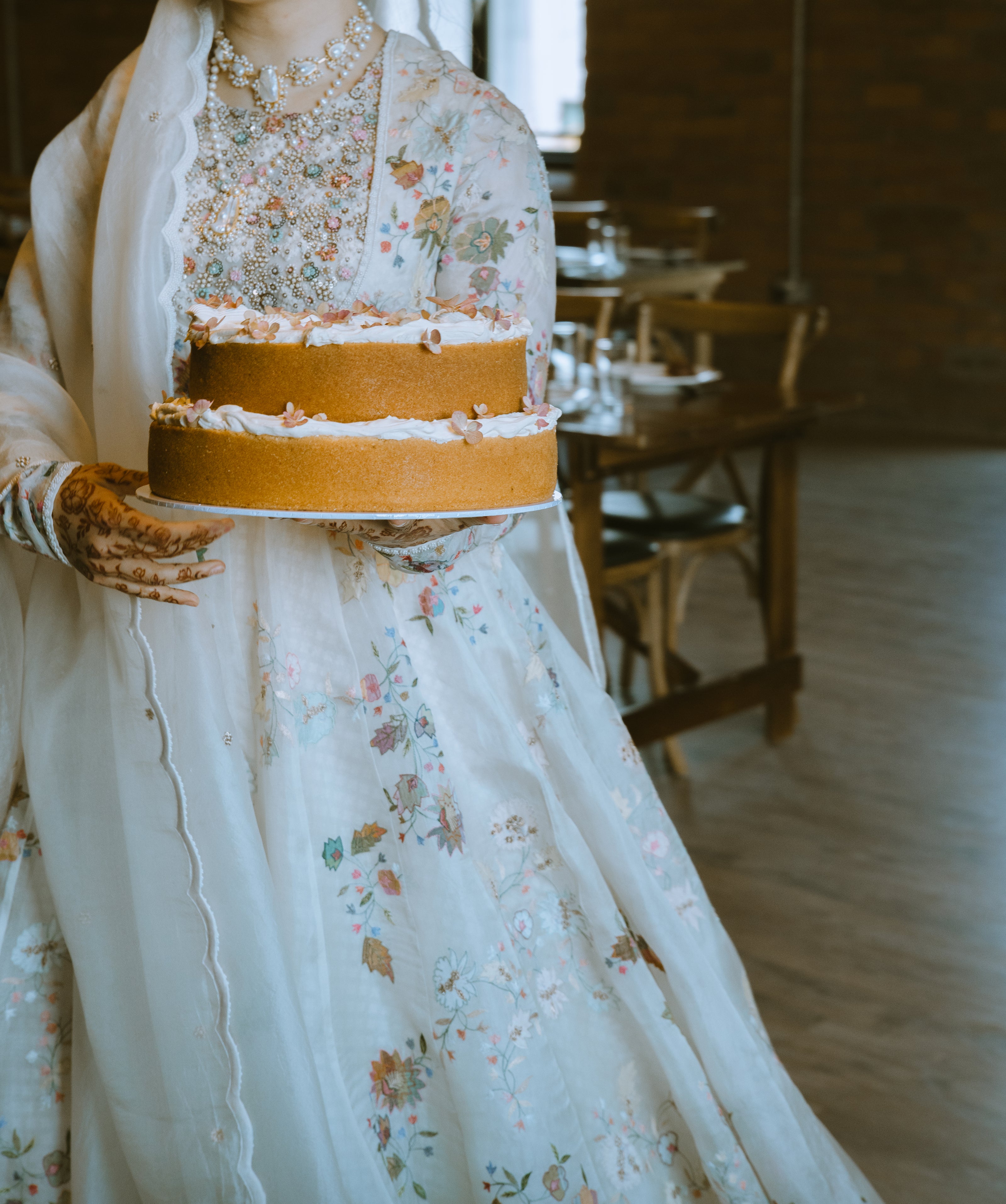 Stunning bride in a floral dress wearing jewellery and holding a wedding cake