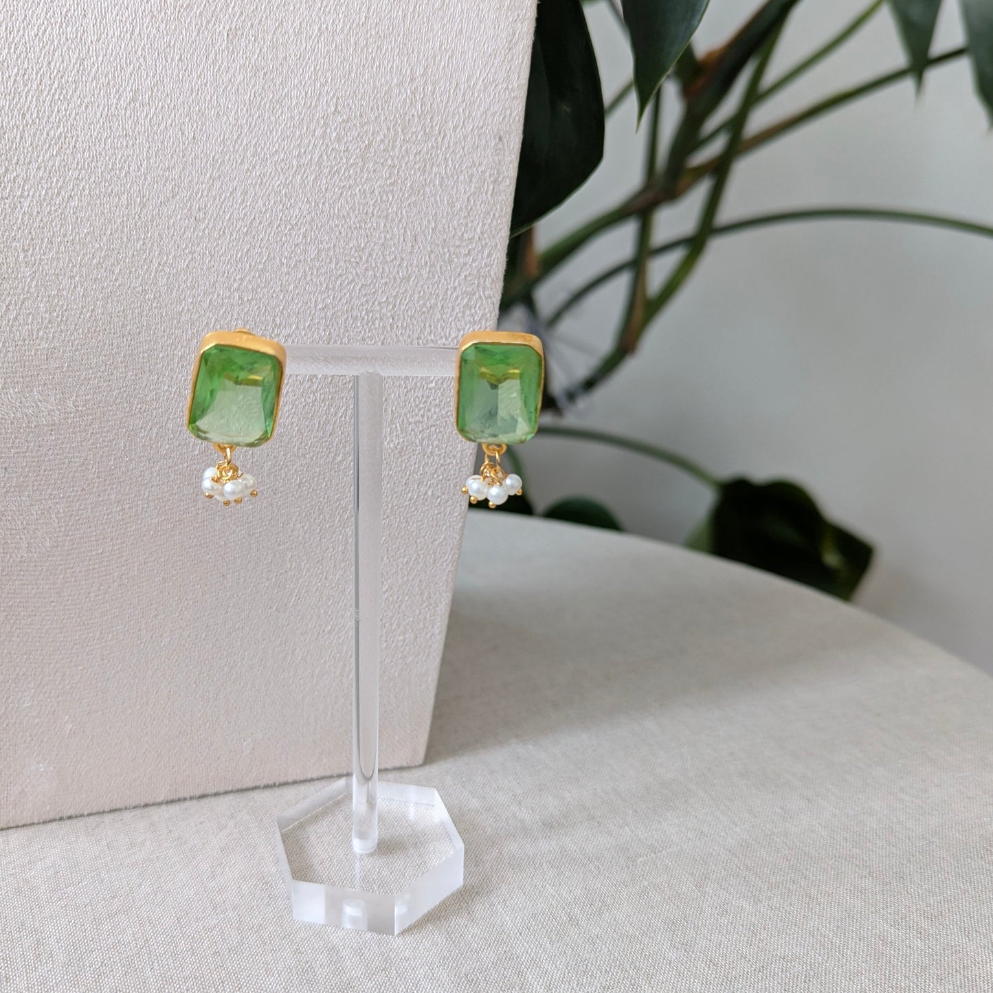 Green square earrings on a clear stand with a neutral background