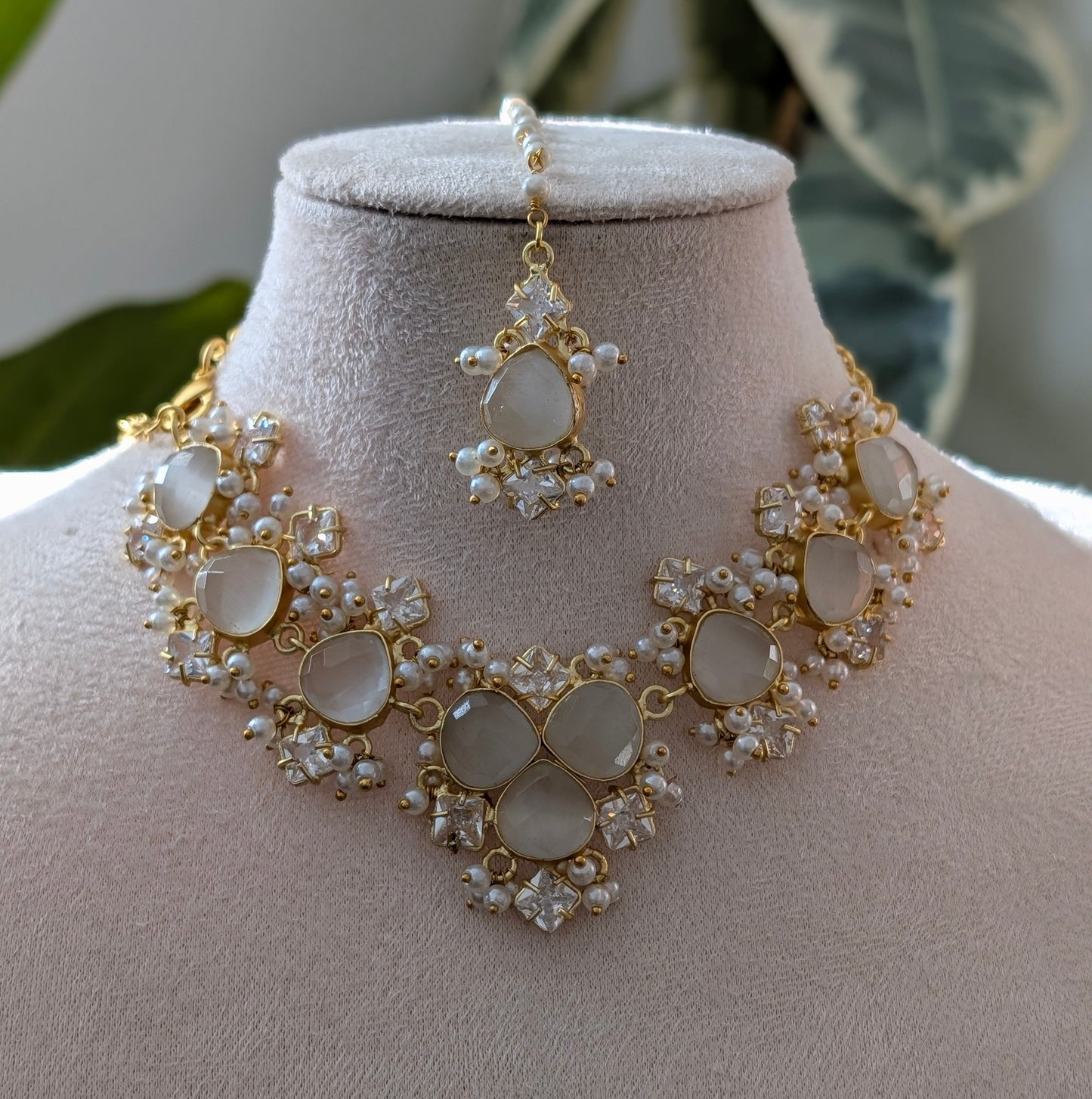 Gold and pearl necklace on a mannequin bust with a blurred plant background