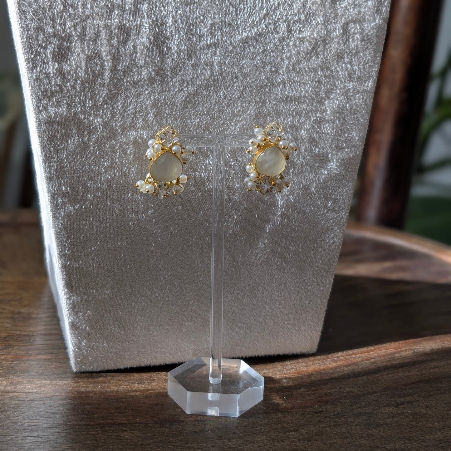 Gold earrings on a clear stand against a textured gray background