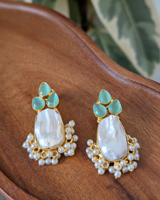 Pair of earrings with green gemstones and pearl details on a wooden surface.