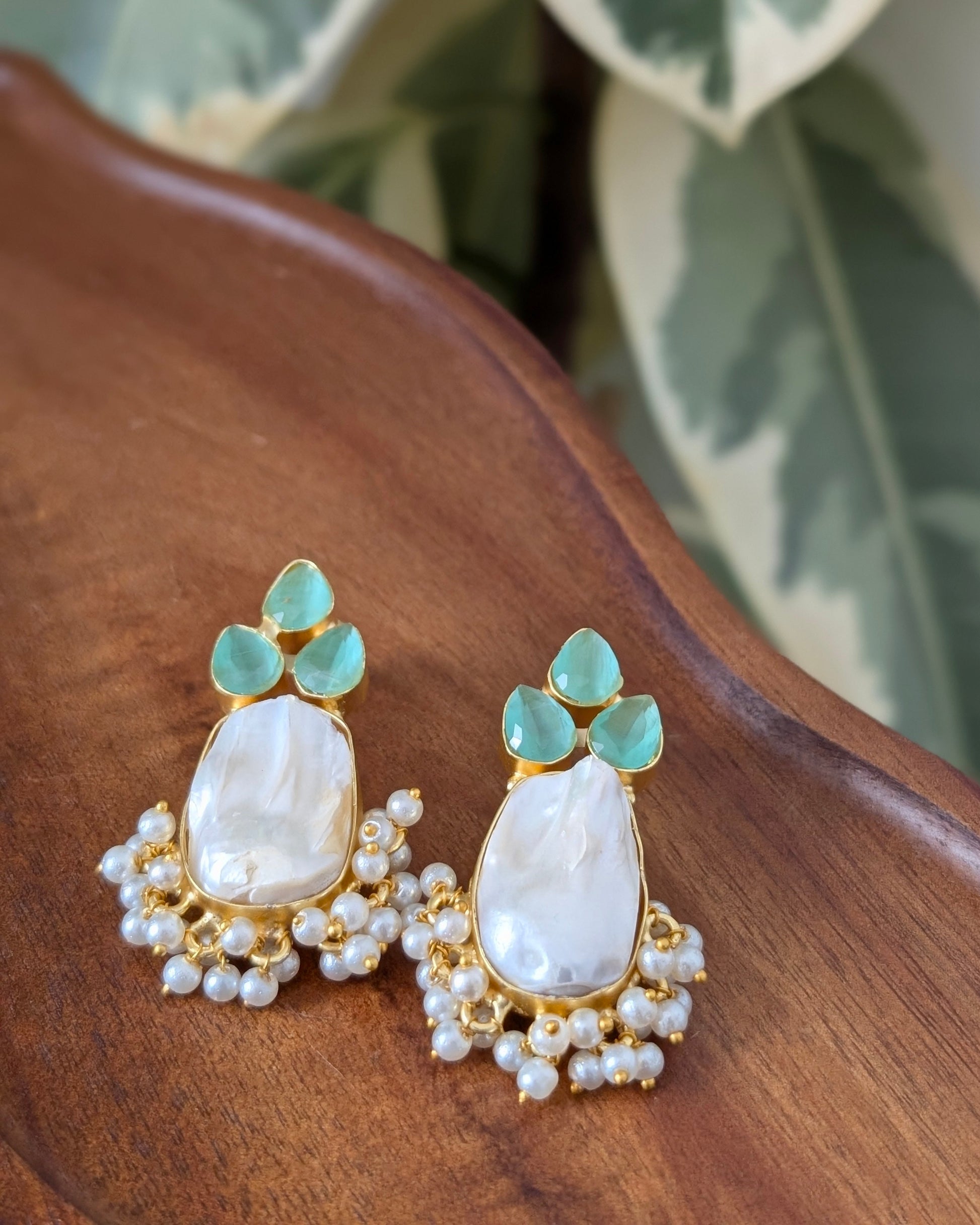 Pair of earrings with green and white stones on a wooden surface with leaves in the background