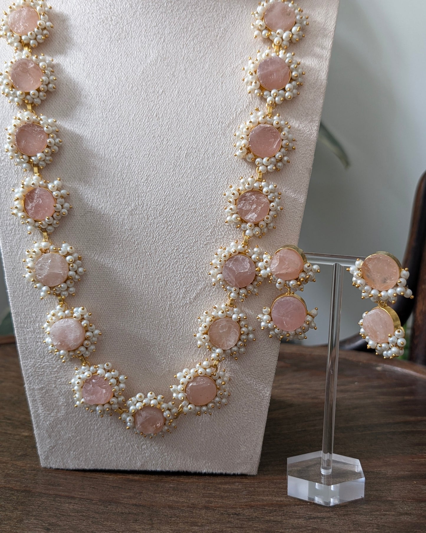 Necklace and earrings with pink stones and pearl-like accents on a stand.