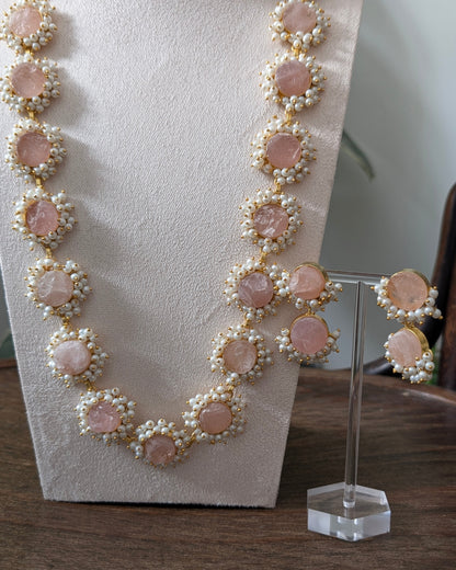 Necklace and earrings with pink stones and pearl-like accents on a stand.