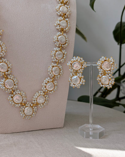 Pearl necklace and earrings on a stand with a neutral background