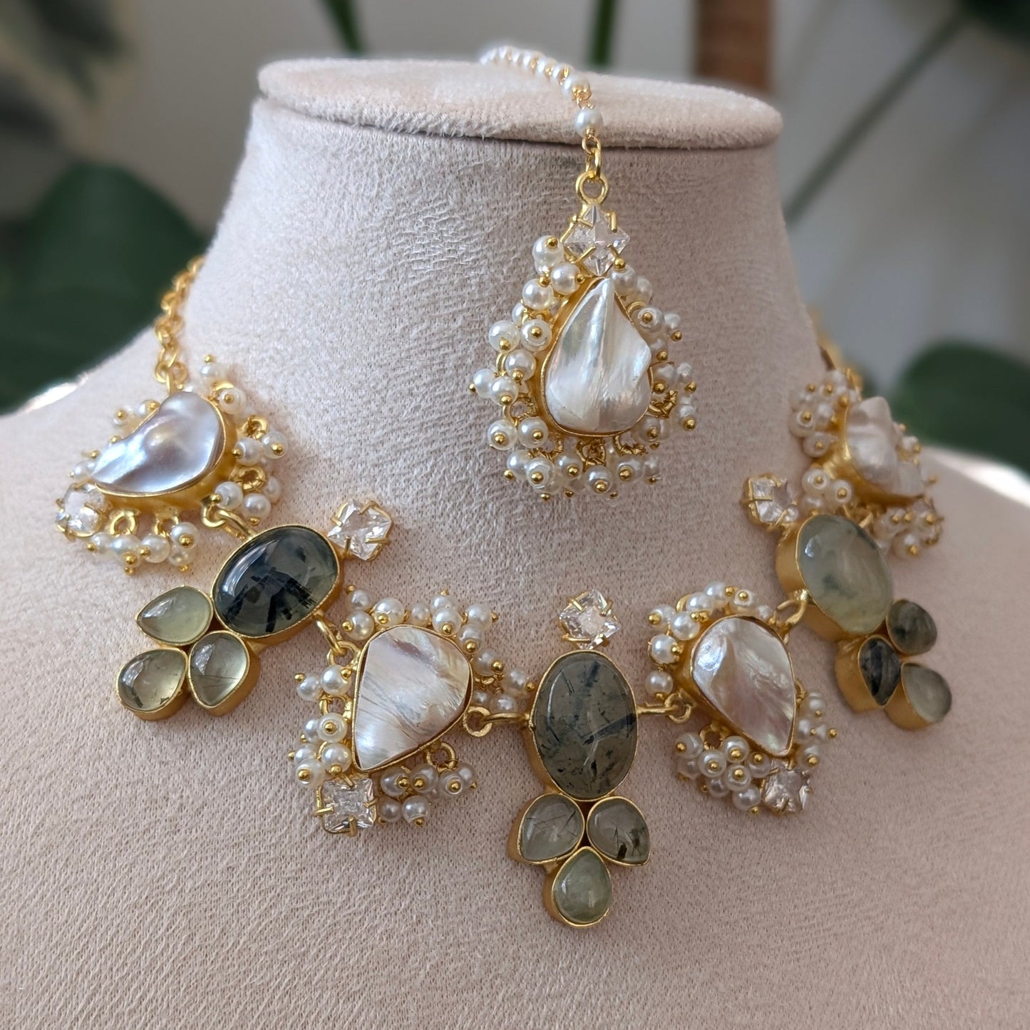 A gold-toned statement necklace set displayed on a beige jewelry bust, featuring large teardrop-shaped mother-of-pearl stones, oval gray marbled stones, and clusters of small white pearls, with a matching drop earring shown above.