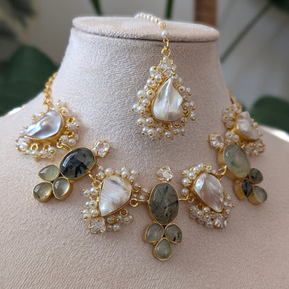 A gold-toned statement necklace set displayed on a beige jewelry bust, featuring large teardrop-shaped mother-of-pearl stones, oval gray marbled stones, and clusters of small white pearls, with a matching drop earring shown above.