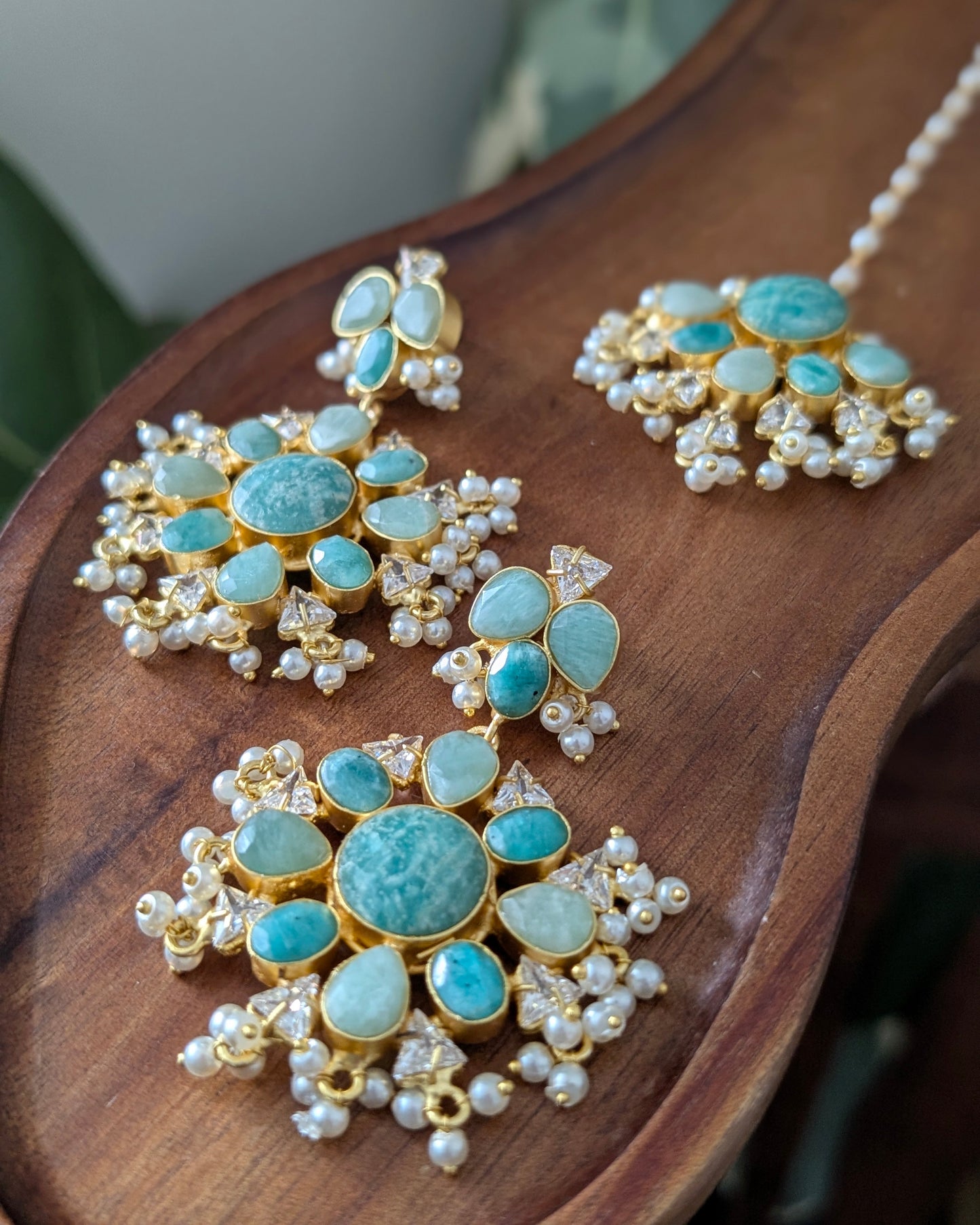Gold-plated jewelry set featuring a mandarin necklace, matching earrings, and a statement piece, embellished with light blue marbled stones and white pearls, displayed on a wooden surface.