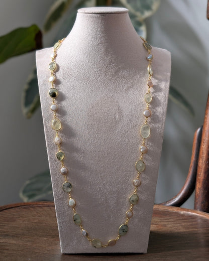 Necklace on a mannequin bust with a blurred plant and wooden object in the background