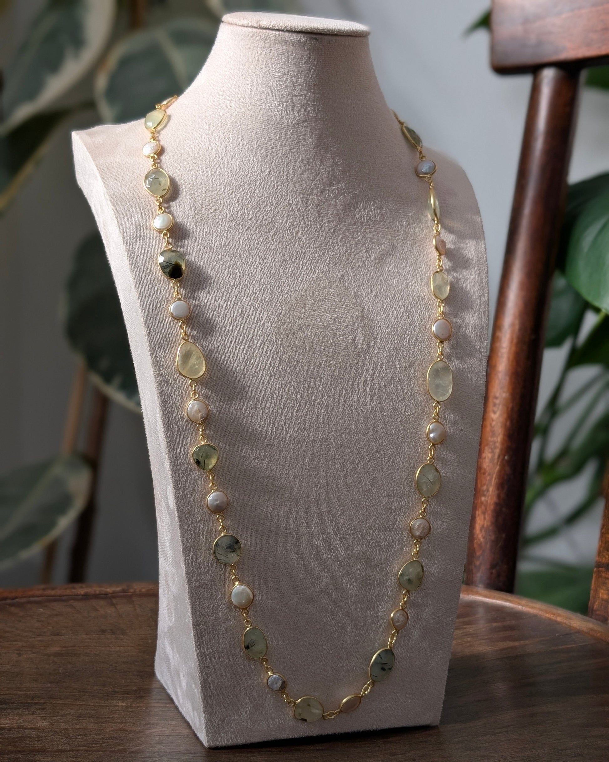 Necklace with green and gold stones on a gray bust against a blurred indoor background