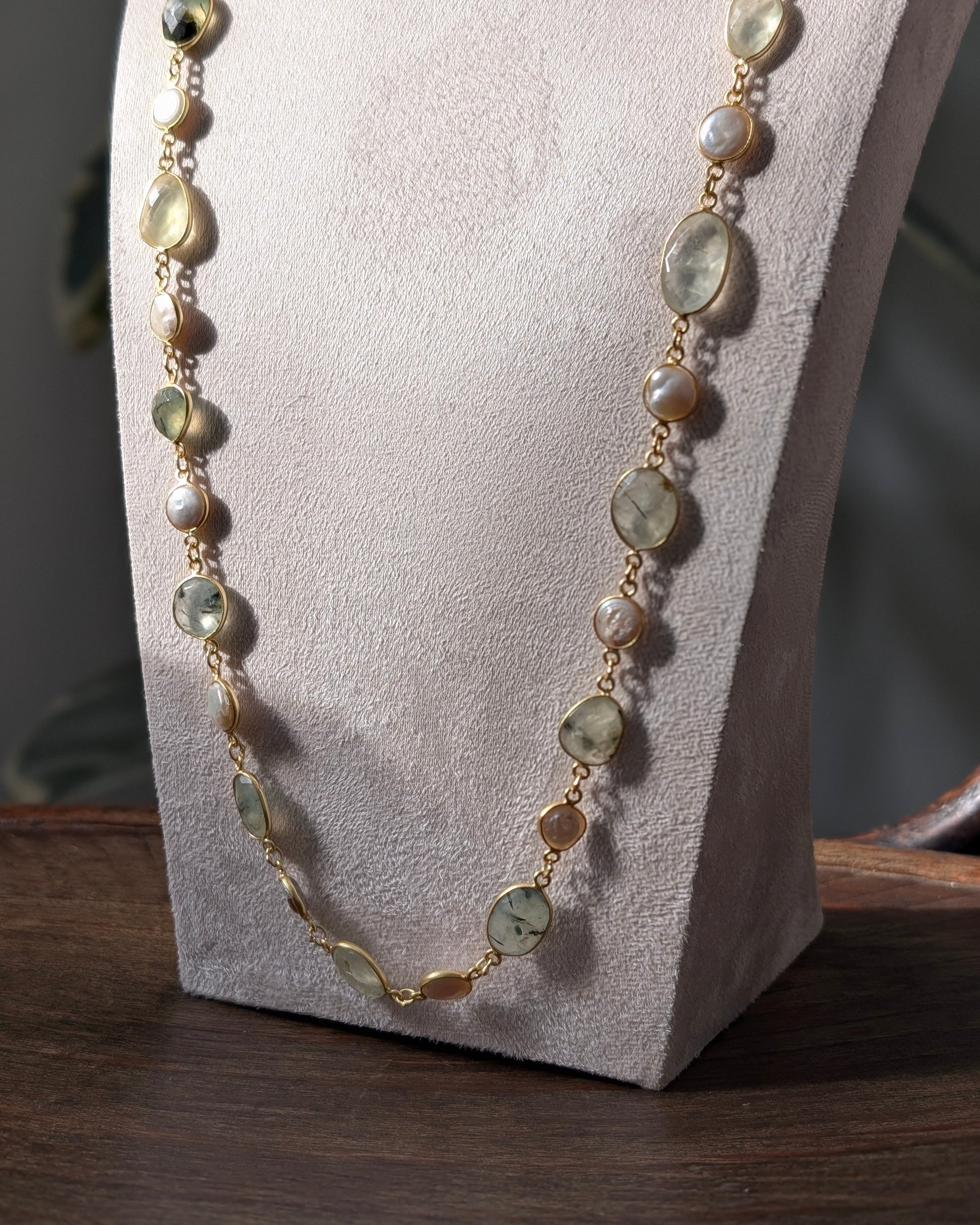 Necklace with green and gold beads on a white stand