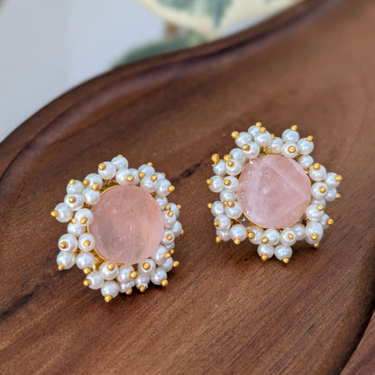 Pair of earrings with pink stones and pearl-like accents on a wooden surface