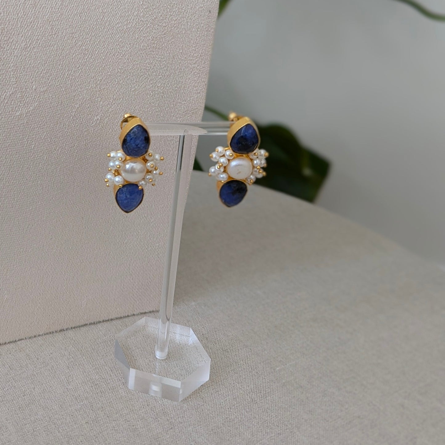 Jewelry set with blue and gold elements on a white stand against a neutral background