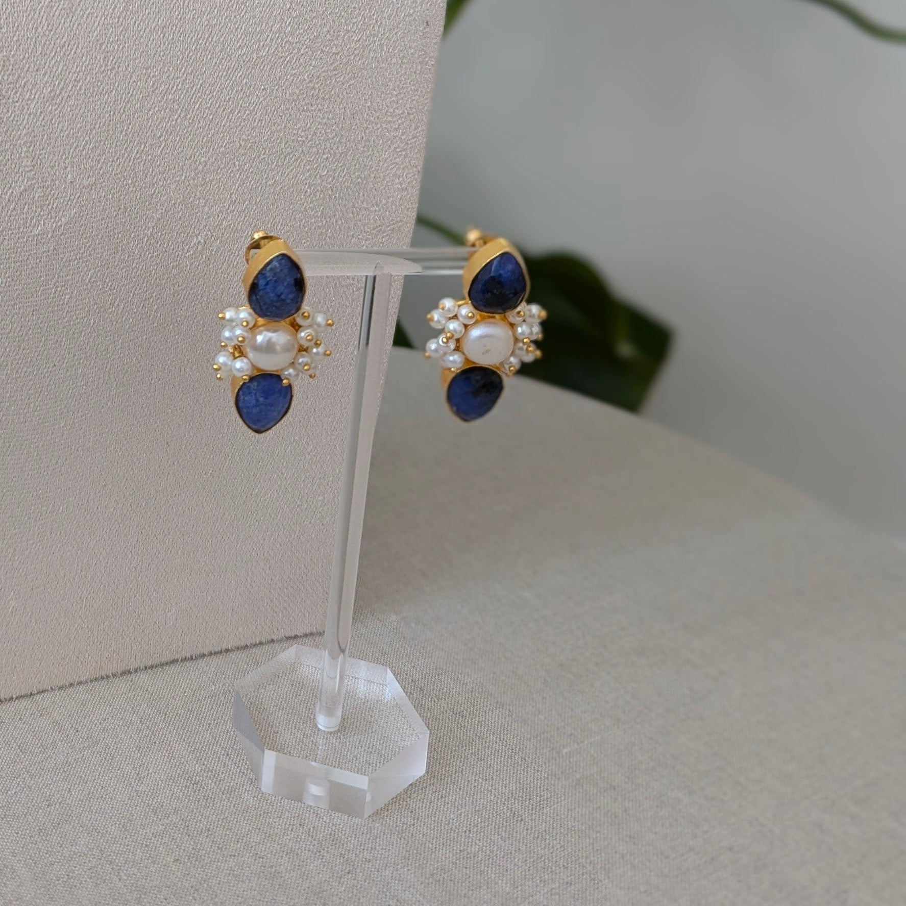 Jewelry set with blue and gold elements on a white stand against a neutral background