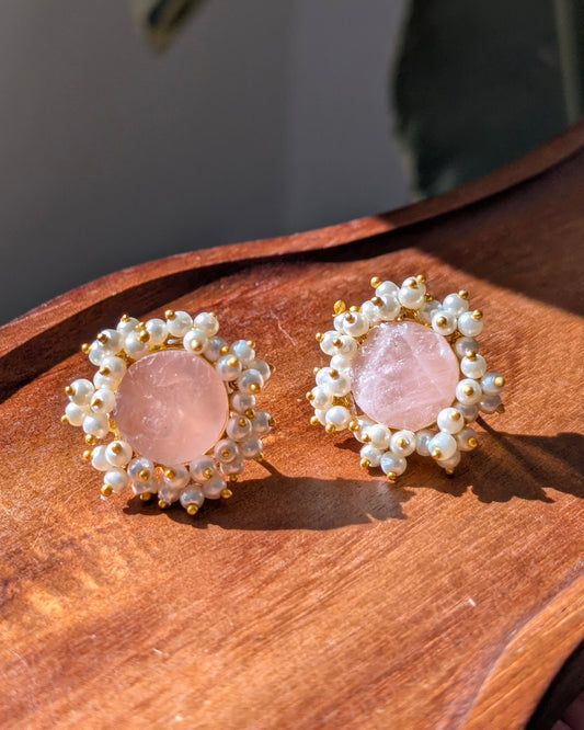 Pair of earrings with pink stones and pearl-like accents on a wooden surface.