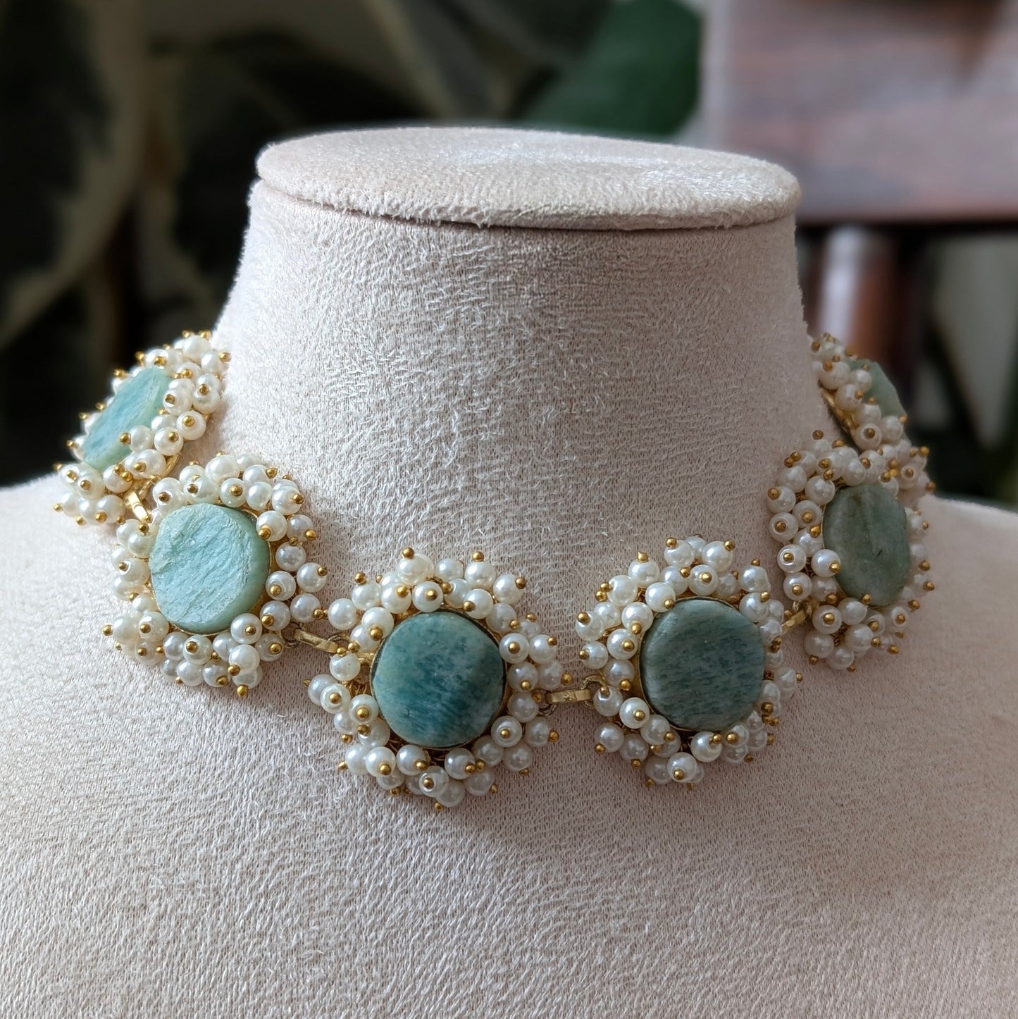A statement collar necklace featuring light blue amazonite stones and white faux pearls, displayed on a cream fabric jewelry bust.