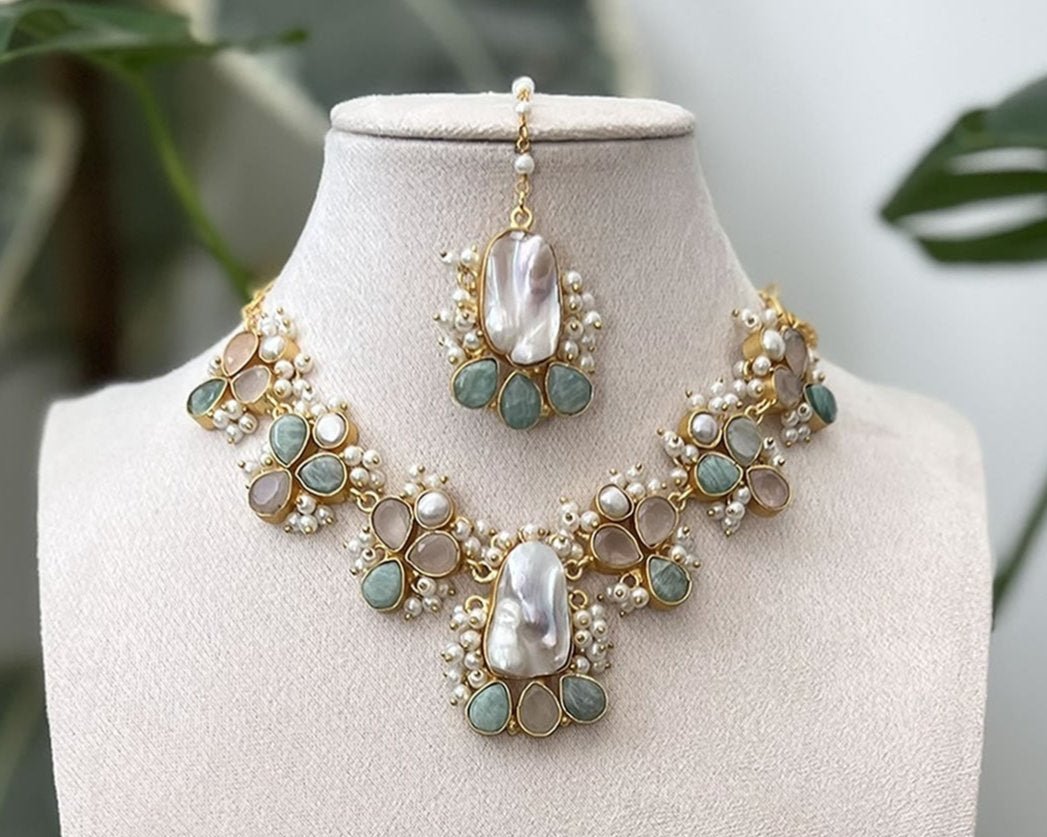 Ethnic jewellery set with mother of pearl tikka and necklace, with hints of green and peach stones, surrounded by pearl clusters.