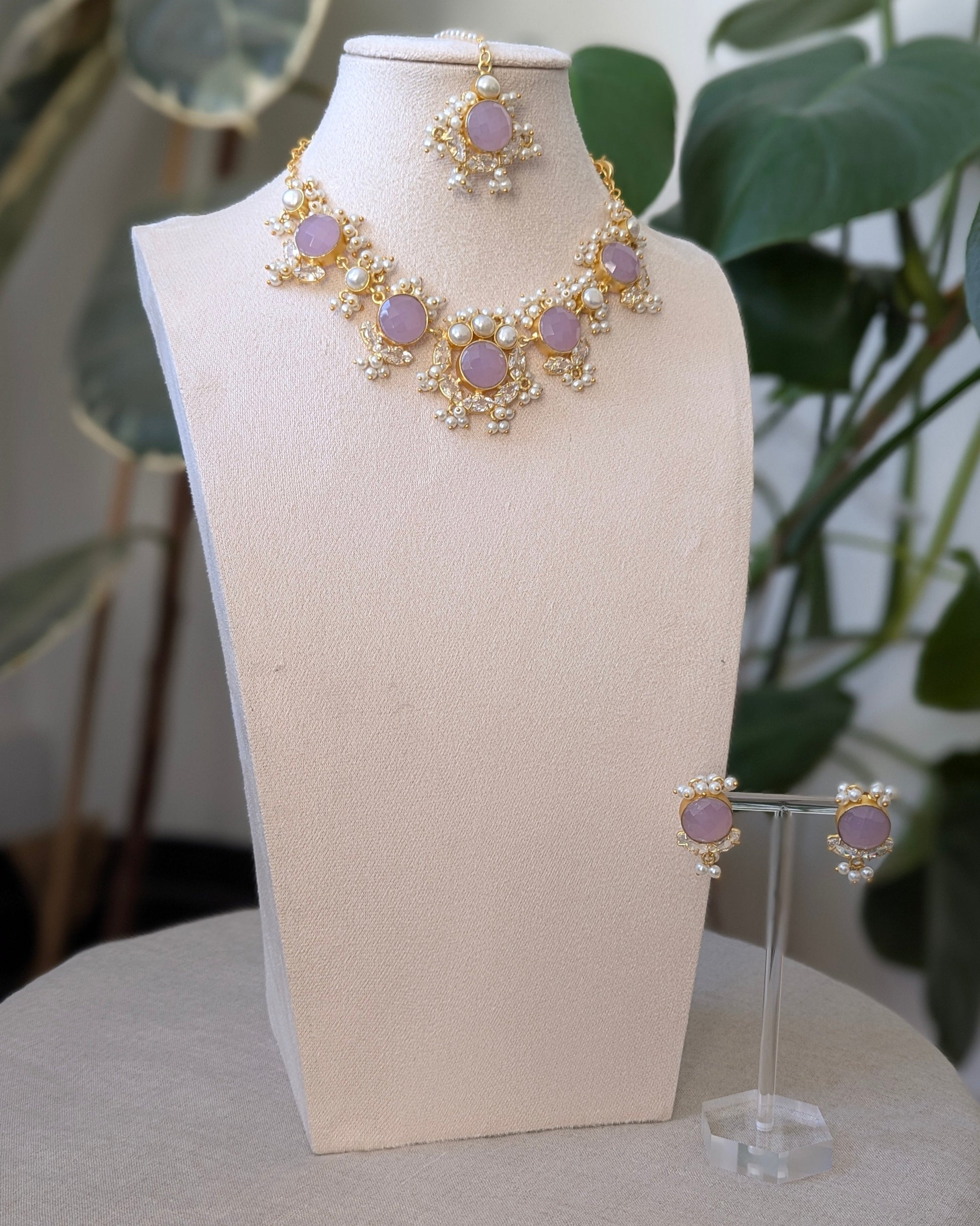 Jewelry set with necklace and earrings on a mannequin bust against a plant-filled background