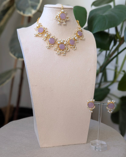 Jewelry set with necklace and earrings on a mannequin bust against a plant-filled background