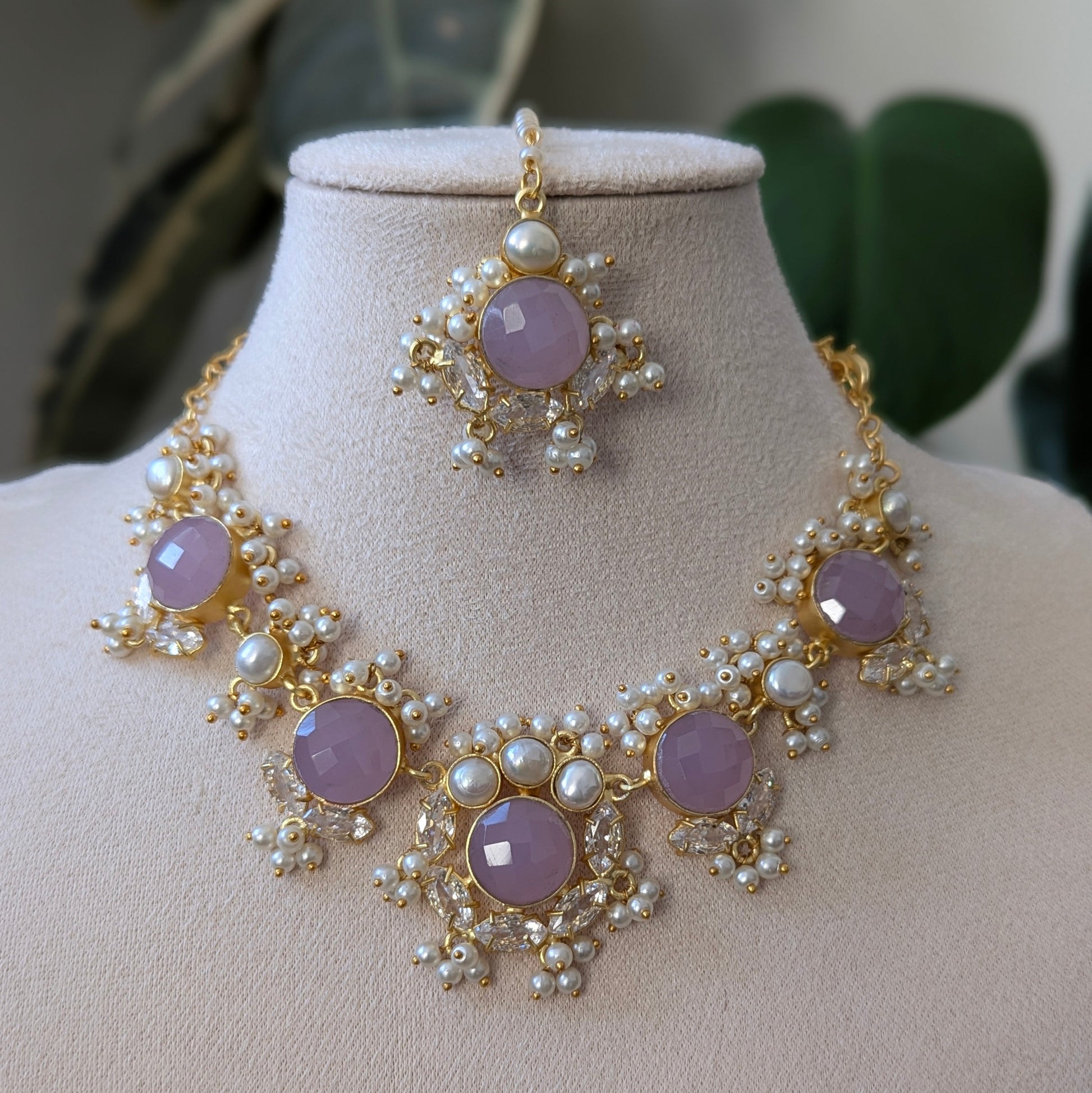 Necklace and earrings set with purple stones and pearl accents on a mannequin bust.