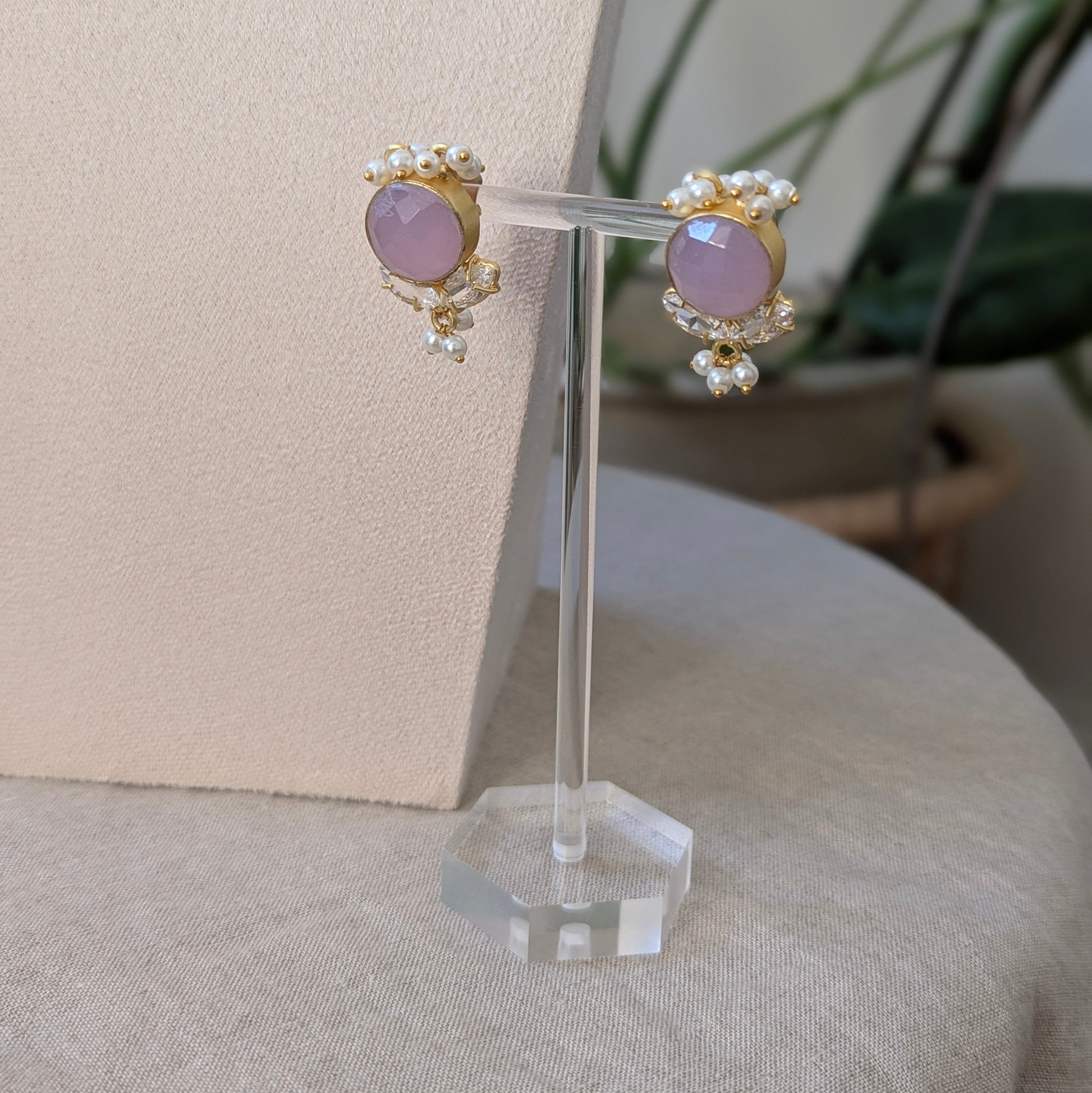 Pair of earrings with purple gemstones on a clear stand against a neutral background