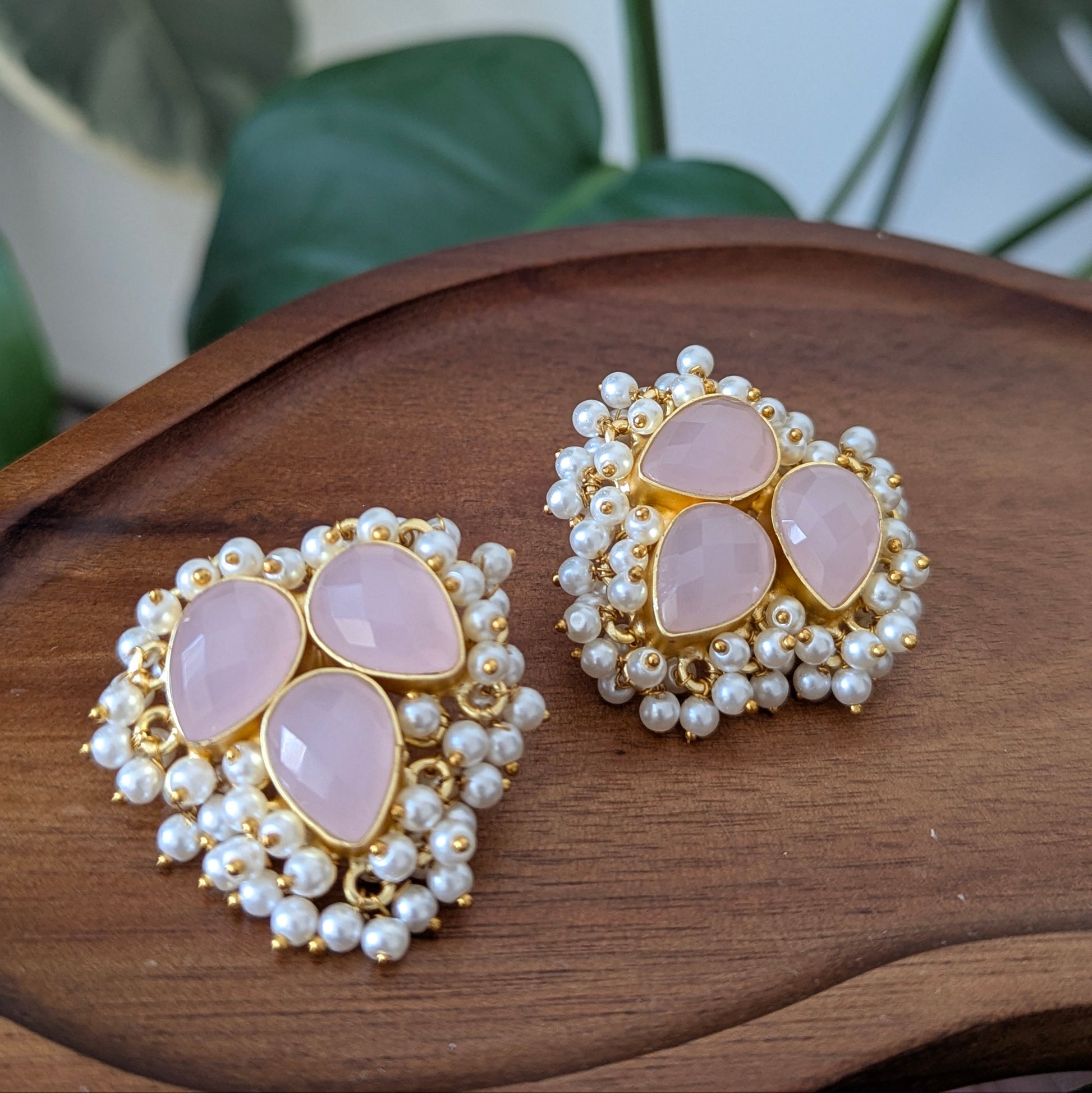 Pair of earrings with pink stones and pearl-like beads on a wooden surface.