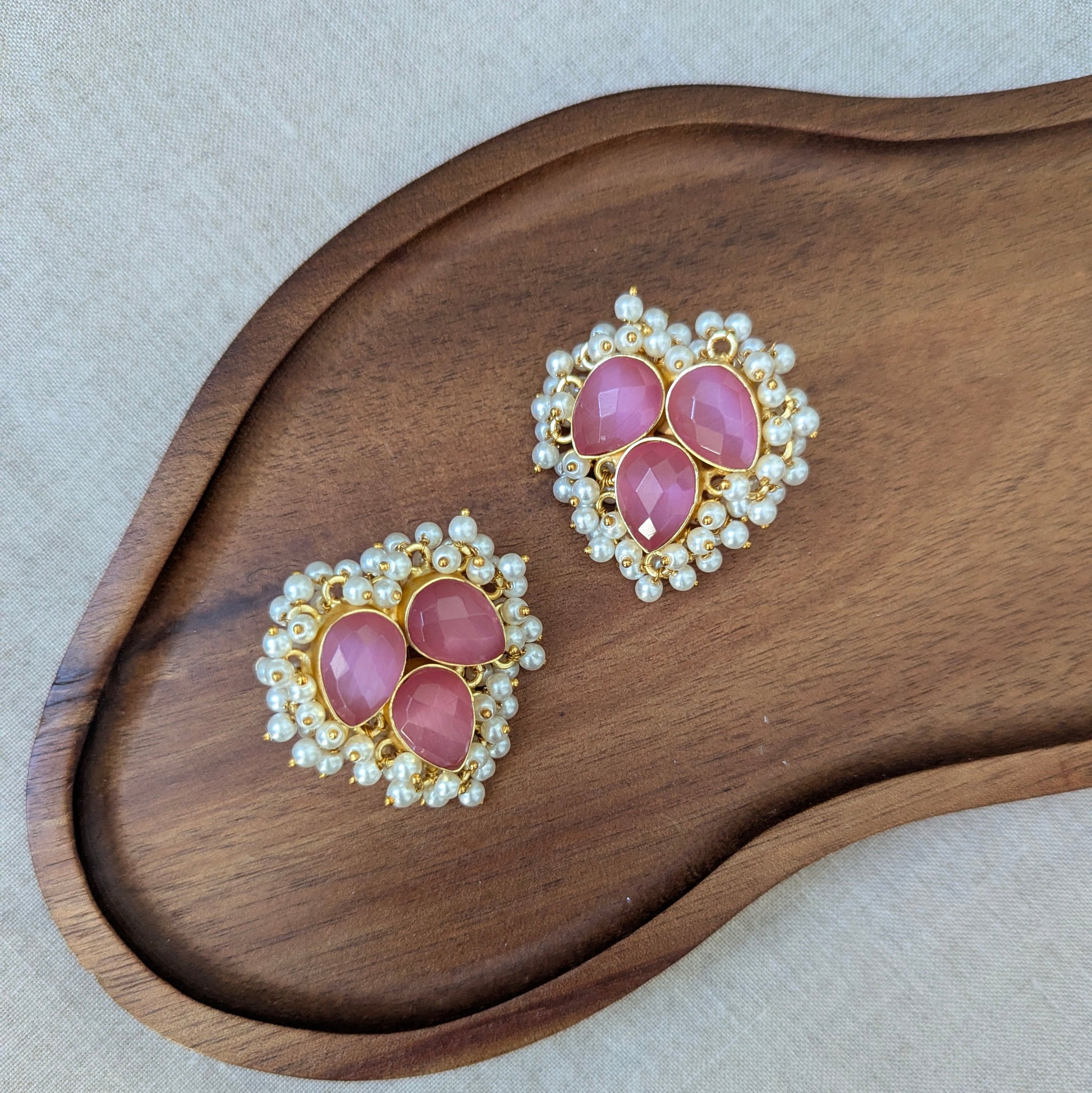 Pair of earrings with pink gemstones and pearl accents on a wooden surface