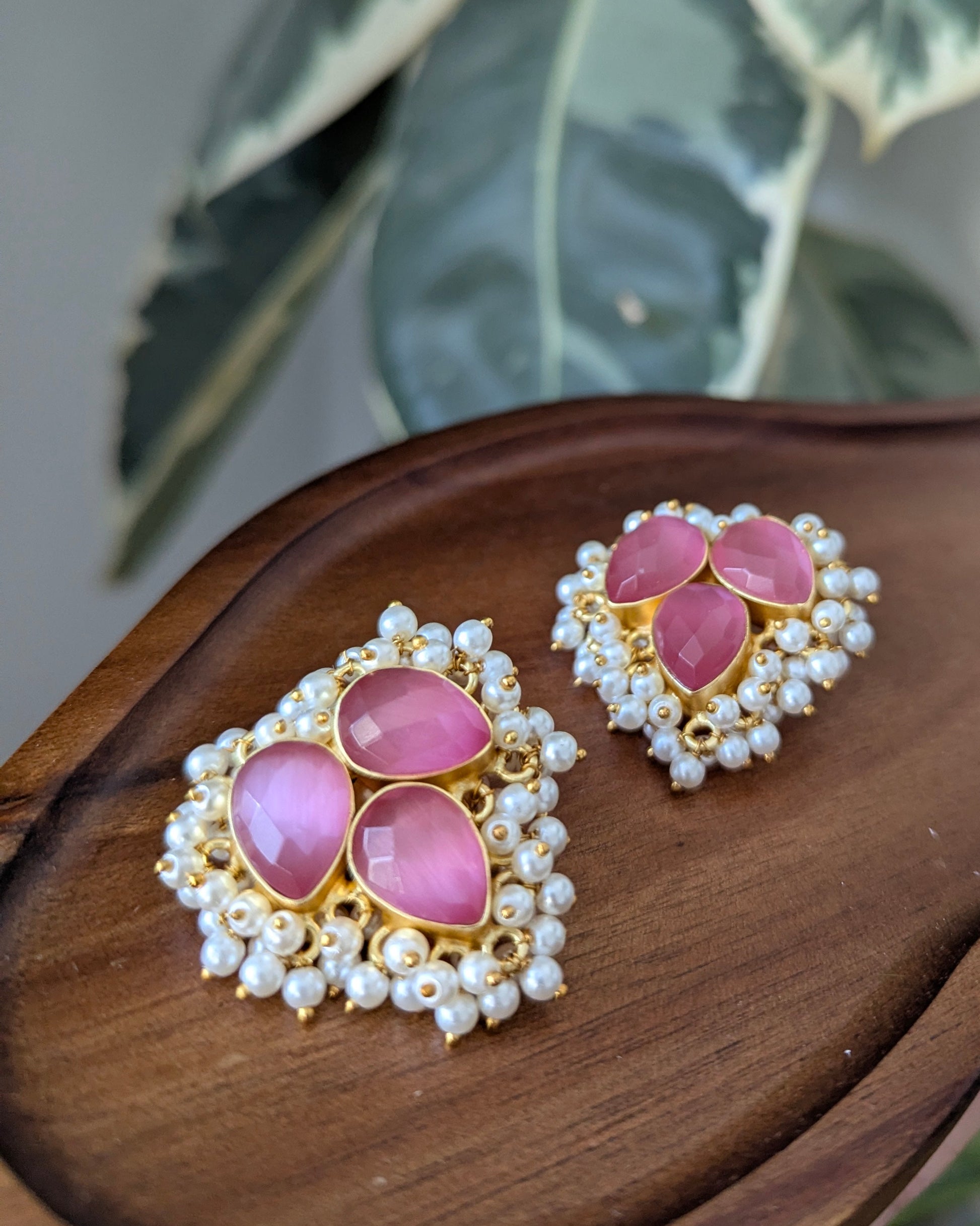 Pink earrings with gold and pearl details on a wooden surface