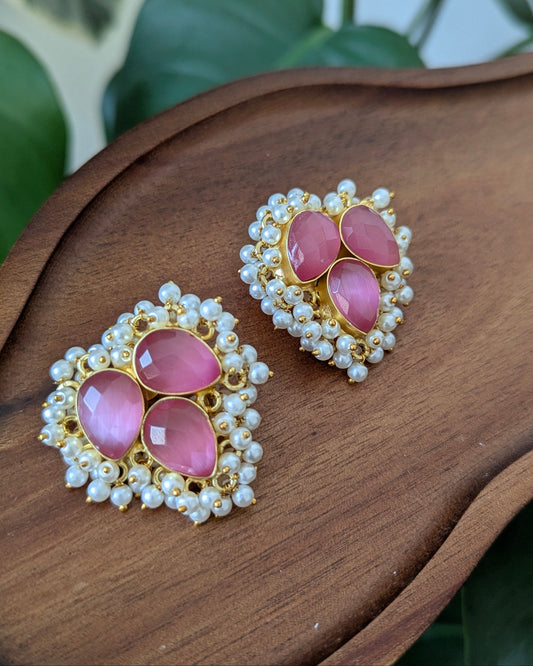 Pair of earrings with pink stones and pearl-like accents on a wooden surface.