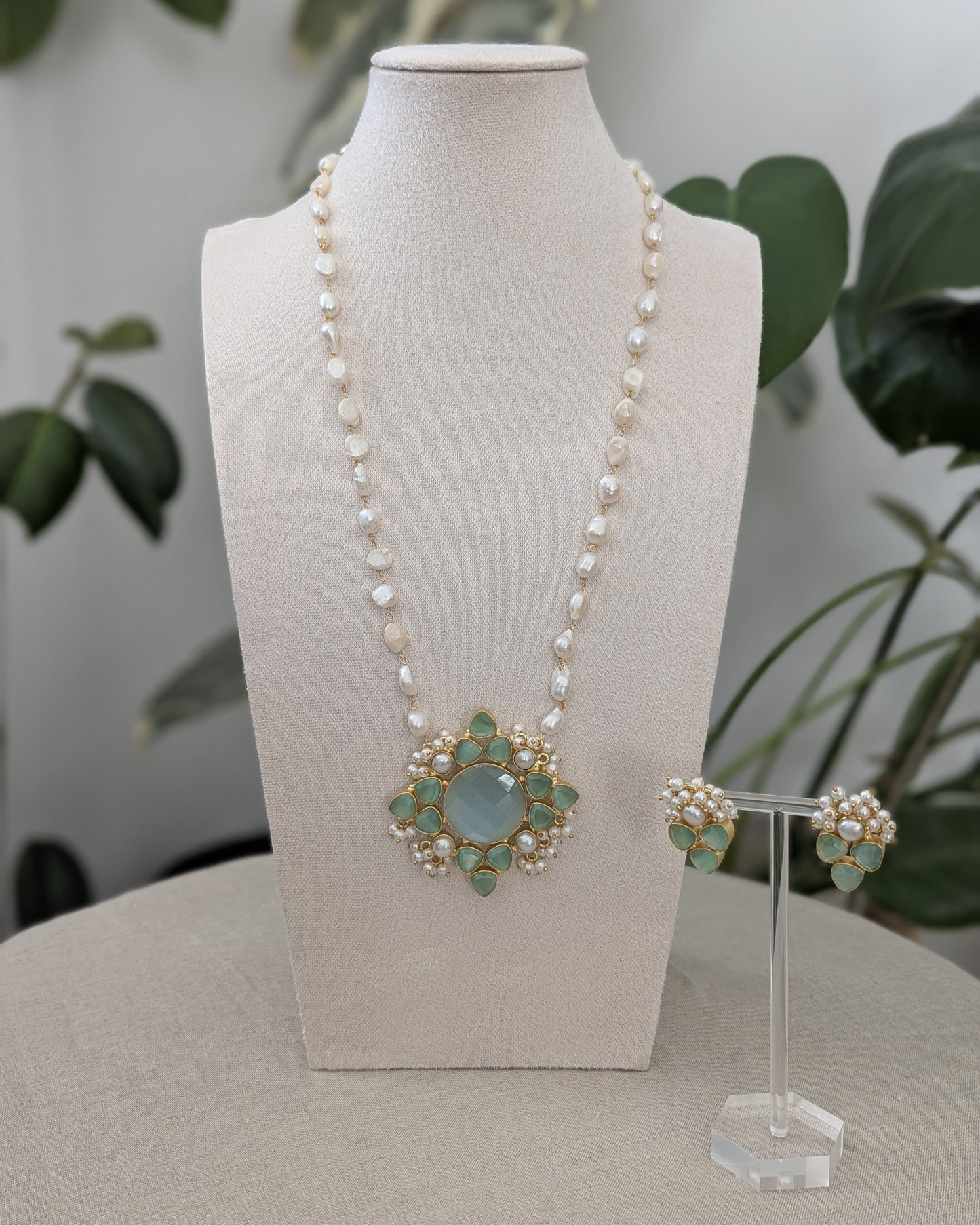 Pearl necklace with a decorative pendant on a mannequin bust, accompanied by matching earrings.
