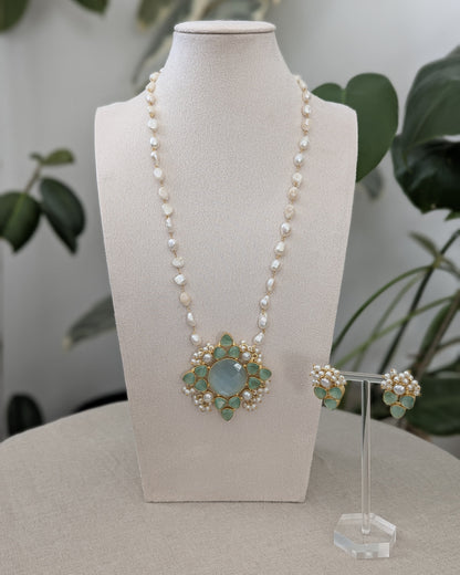 Pearl necklace with a decorative pendant on a mannequin bust, accompanied by matching earrings.