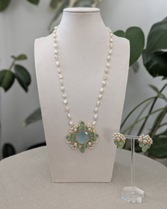 Pearl necklace with a decorative pendant on a mannequin bust, accompanied by matching earrings.