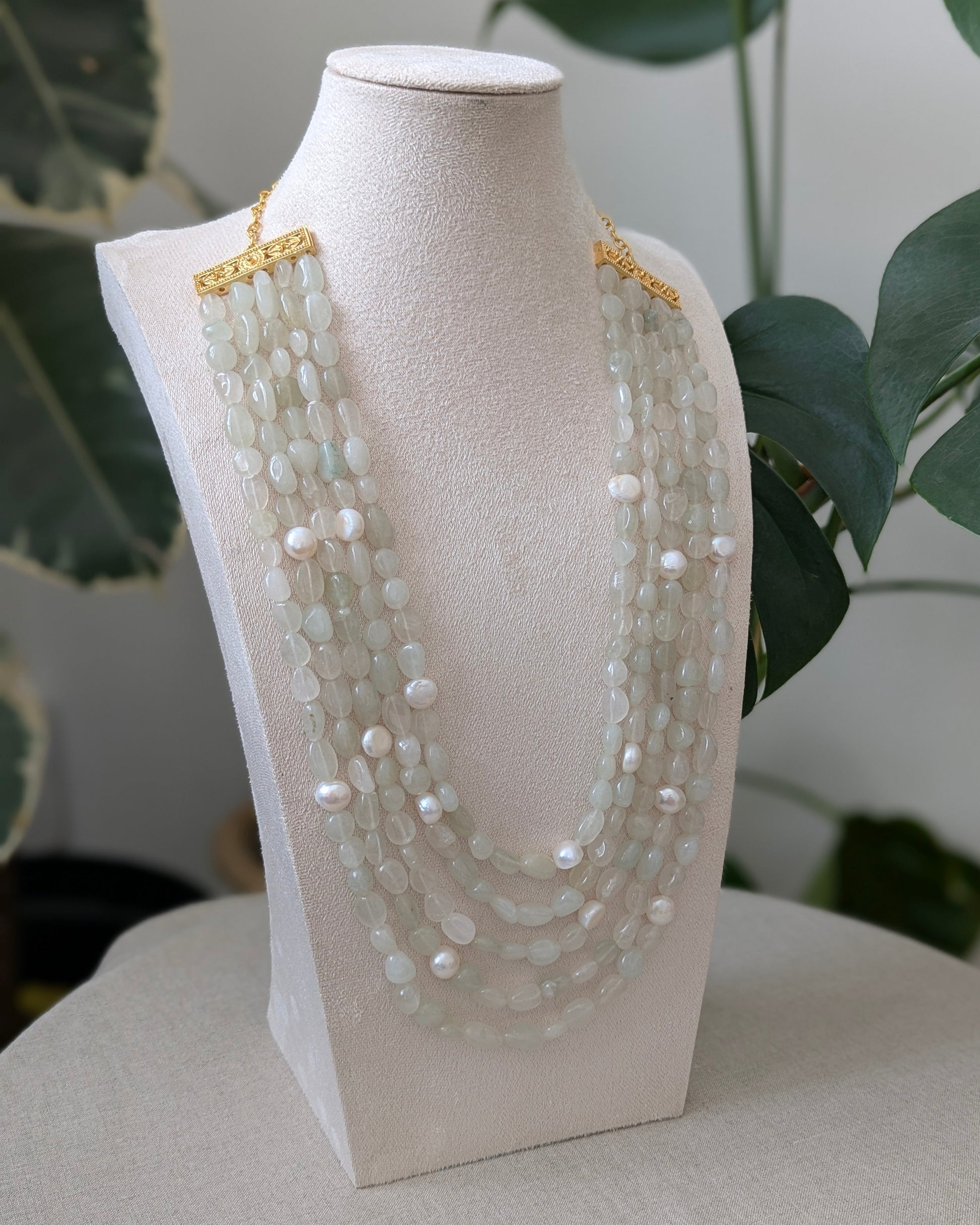 Multi-strand pearl necklace on a white mannequin bust with a blurred green plant background