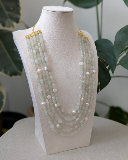 Multi-strand pearl necklace on a white mannequin bust with a blurred green plant background