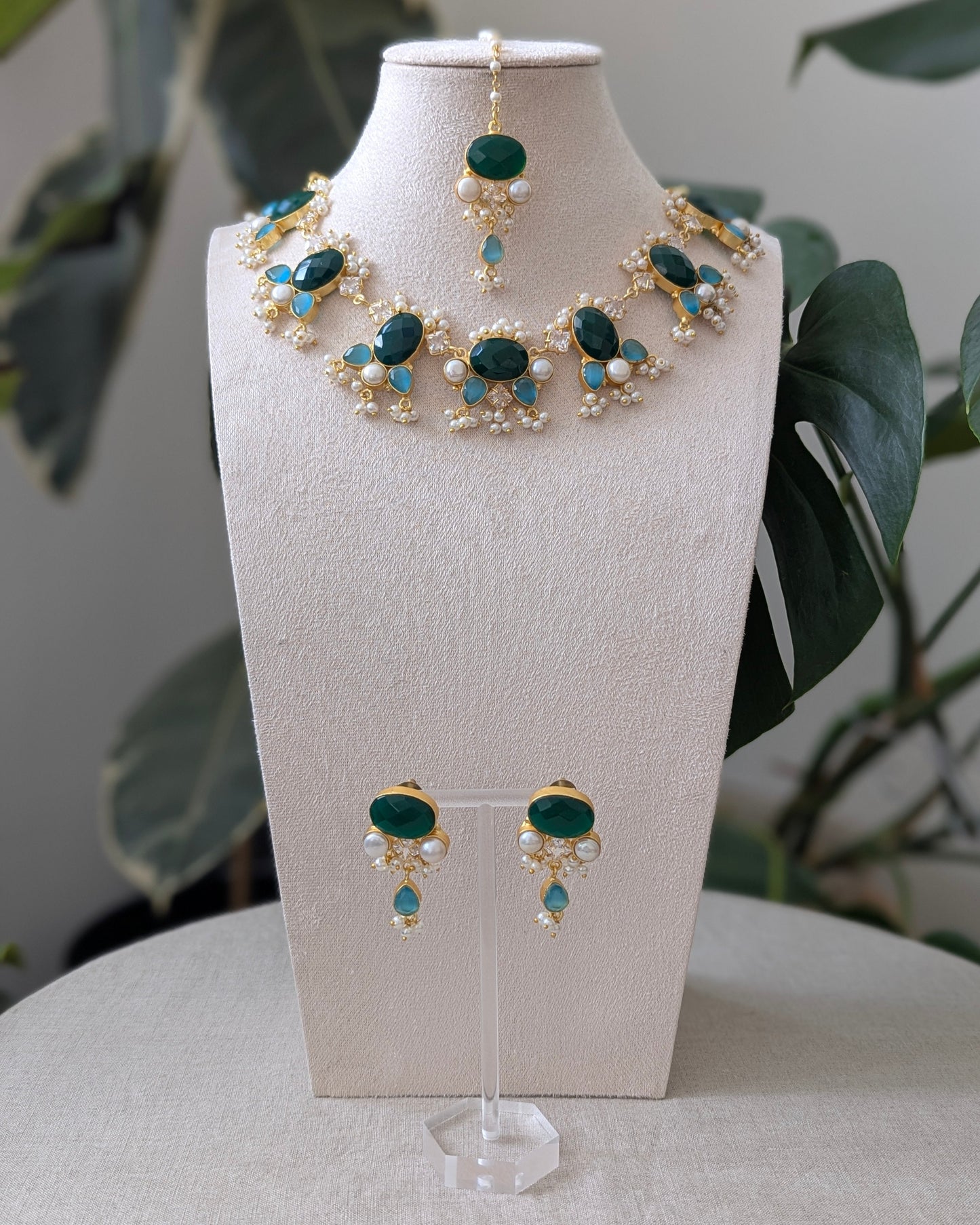 Jewelry set with necklace and earrings on a white stand with green leaves in the background
