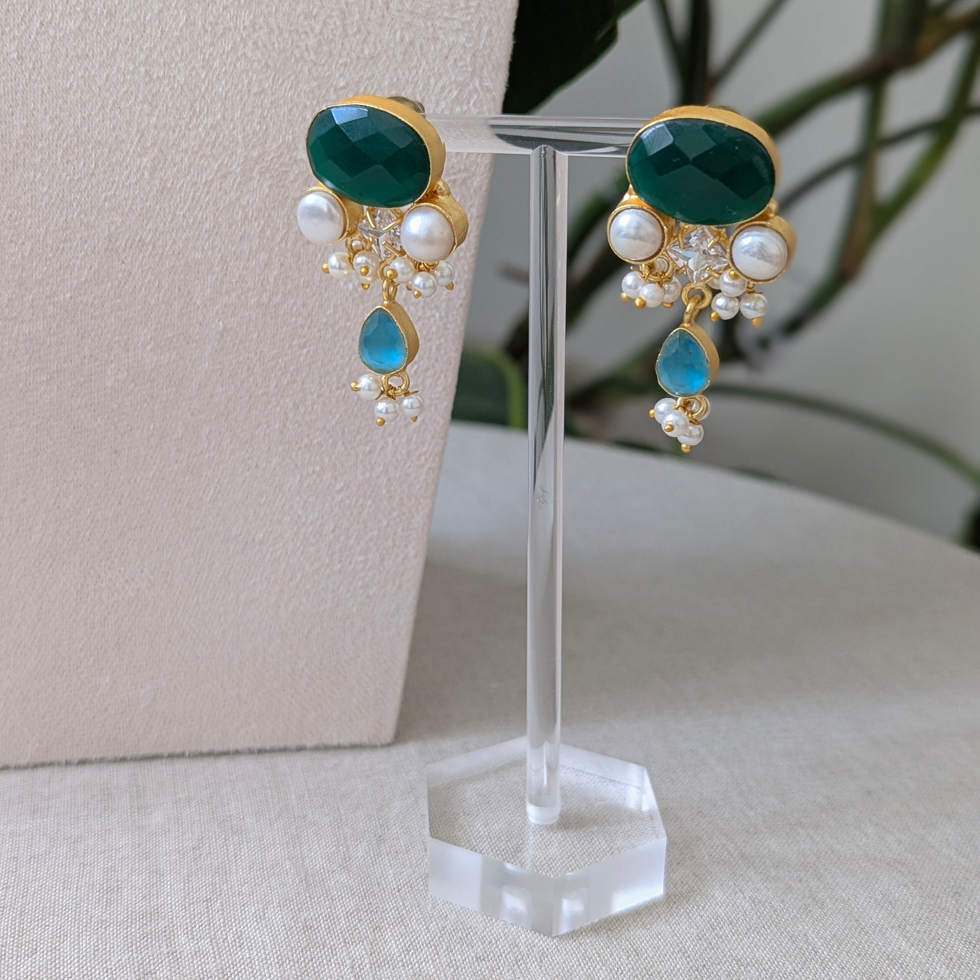 Pair of earrings with green and blue stones on a clear stand against a neutral background