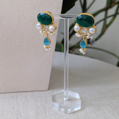 Pair of earrings with green and blue stones on a clear stand against a neutral background