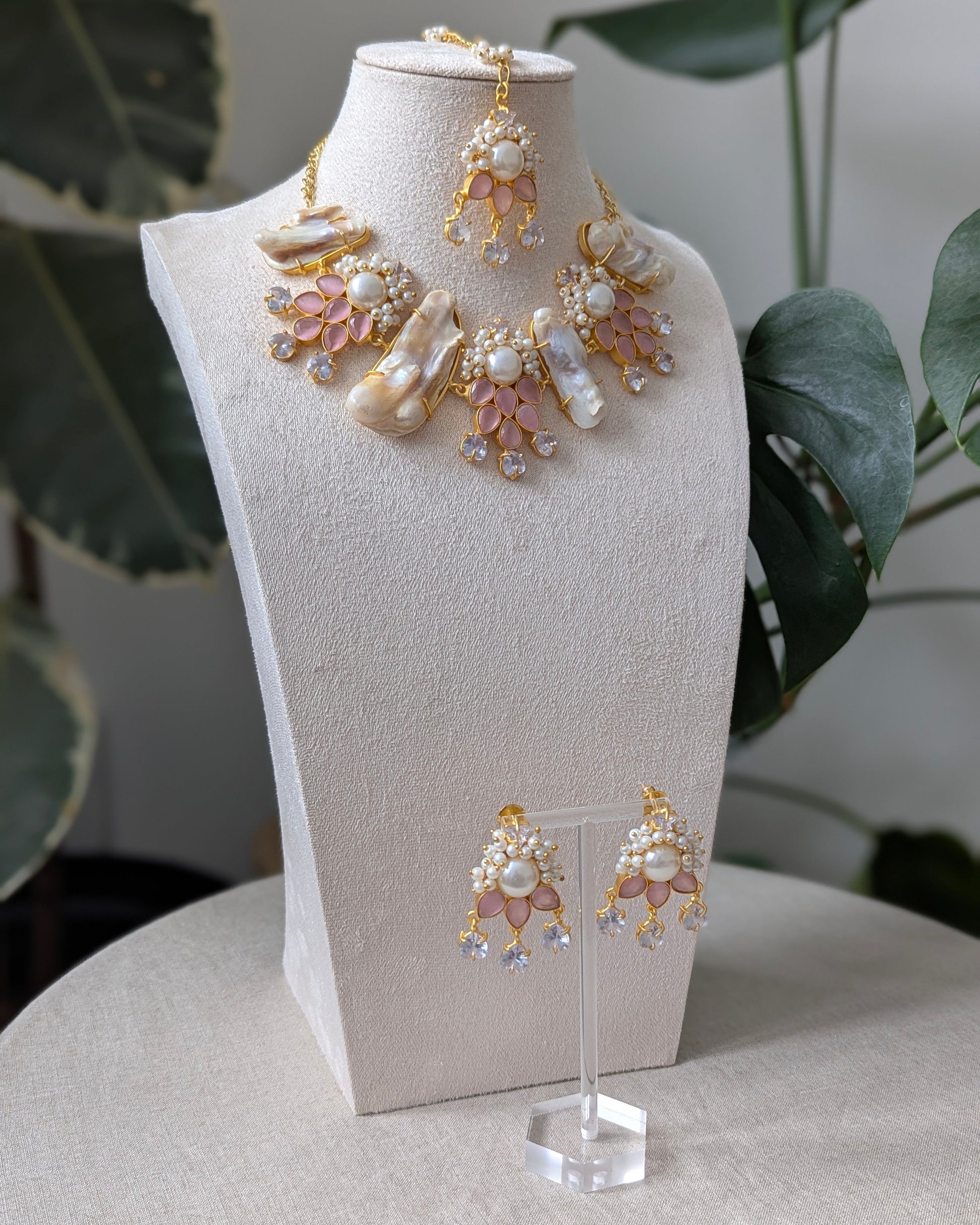 Jewelry set including necklace and earrings on a mannequin bust with plants in the background