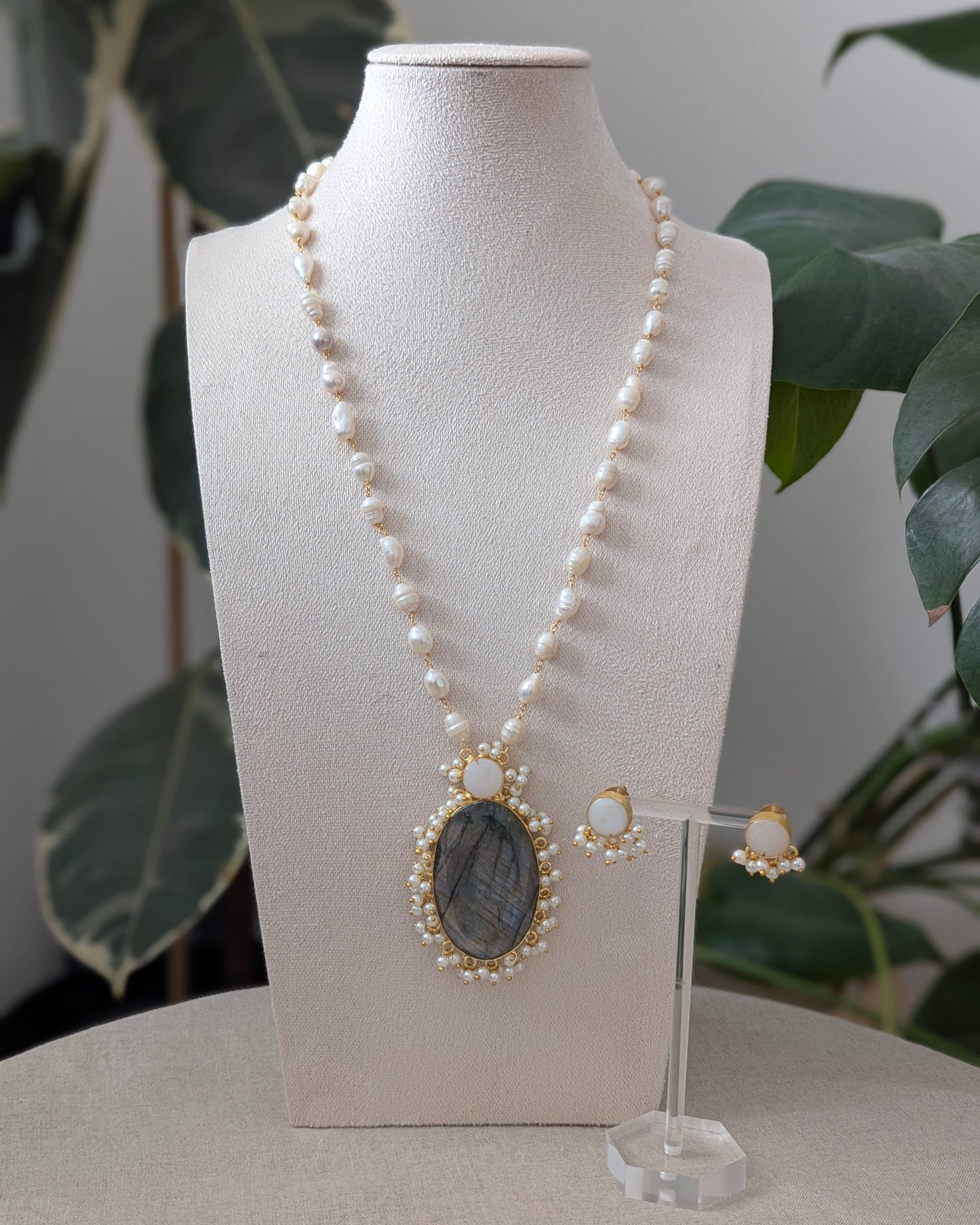 Pearl necklace with pendant and earrings on a mannequin bust with a plant in the background