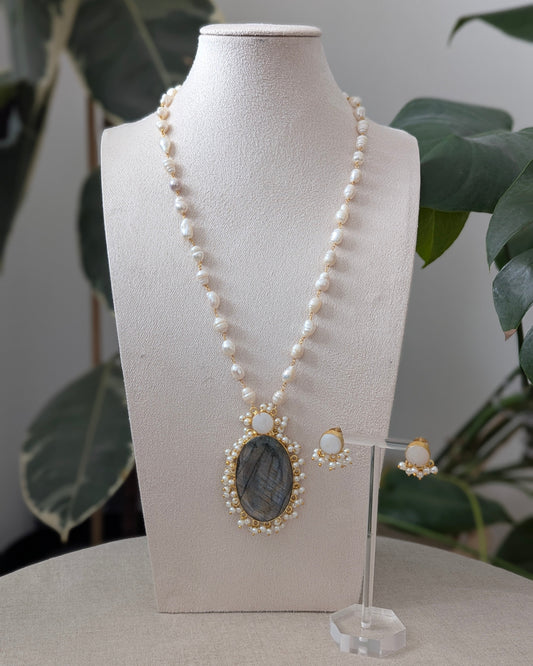 Pearl necklace with pendant and earrings on a mannequin bust with a plant in the background
