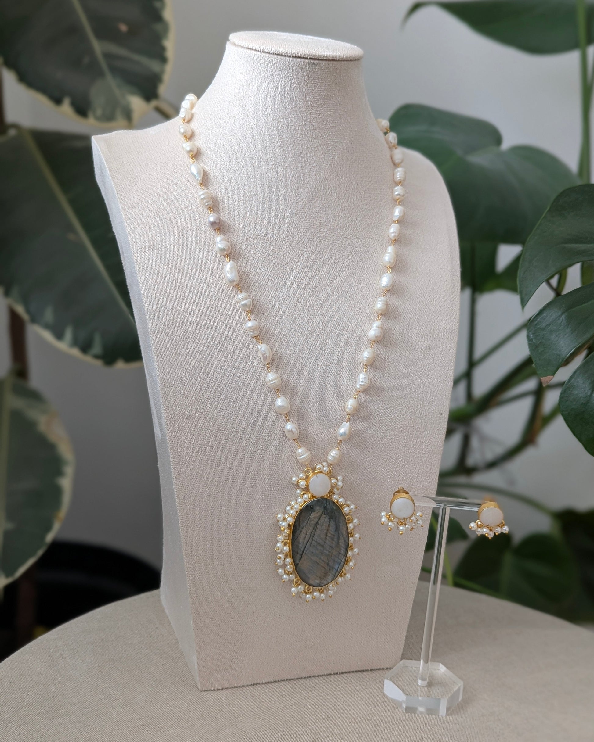 Pearl necklace with a pendant on a mannequin bust with a plant in the background