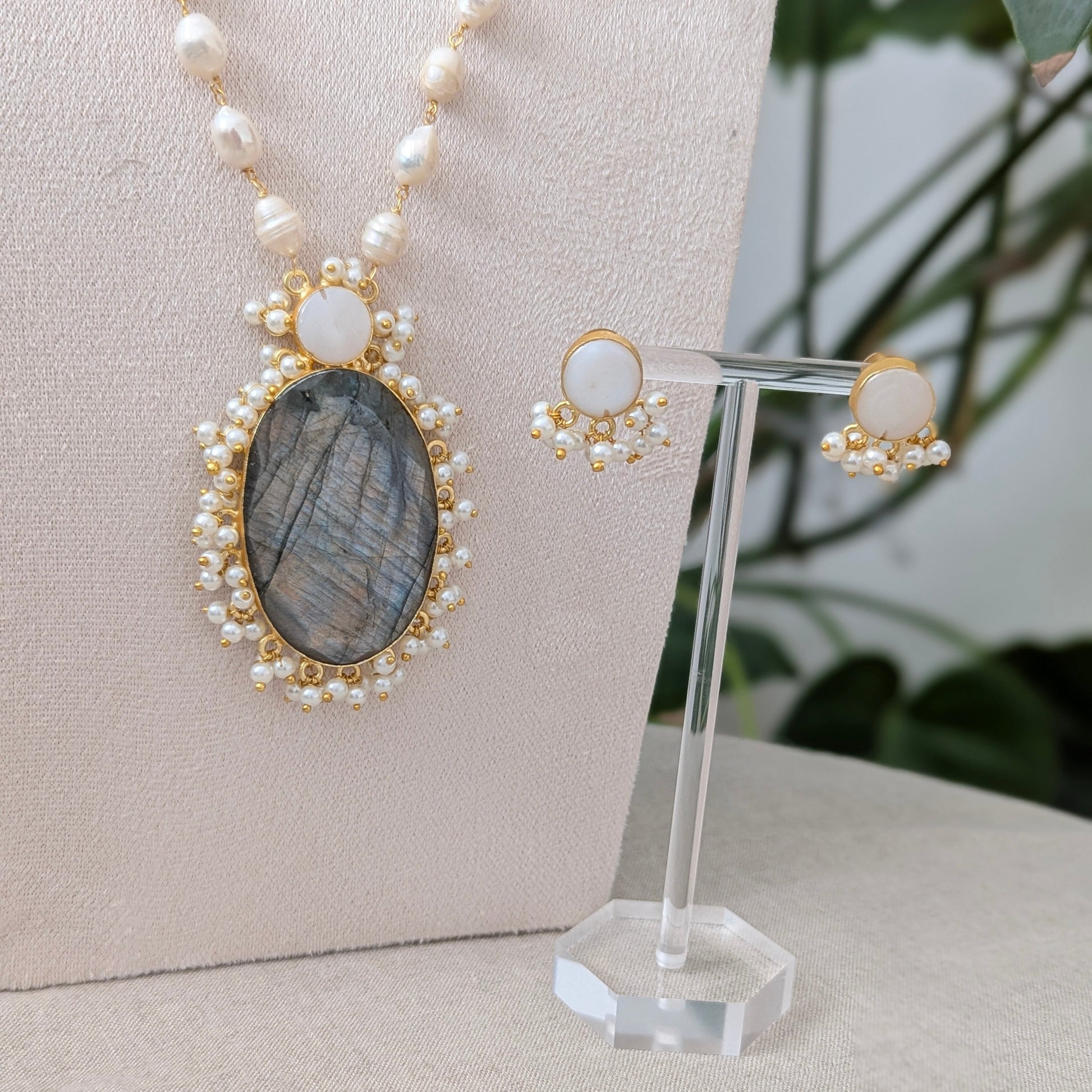 Necklace and earrings with labradorite stone on a stand against a neutral background