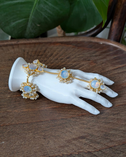 Gold-toned traditional Indian jewelry set with light blue opal stones and pearl-like accents, displayed on a white mannequin hand over a wooden surface with green leaves in the background.